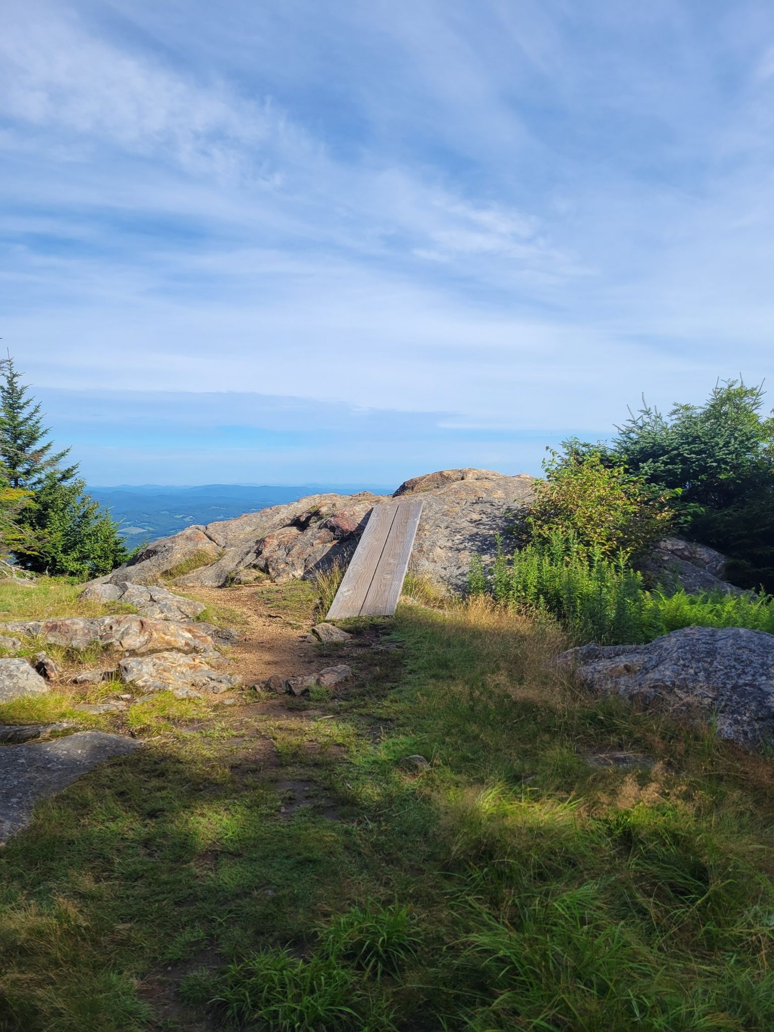 Rocky mountain summit with a wooden plank, blue sky, and distant landscape. - Weathersfield Trail