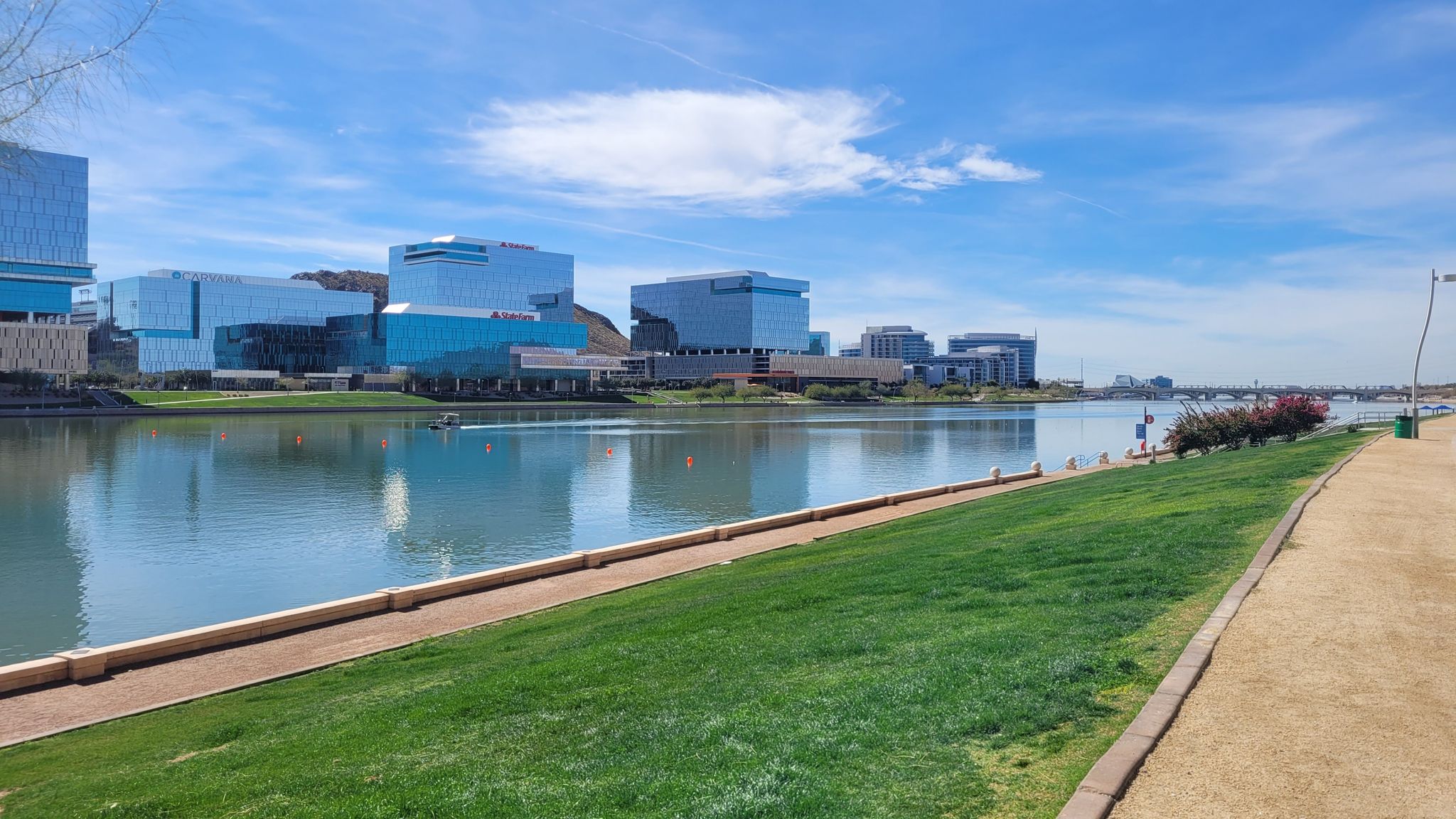 Wide lake with green lawn and modern buildings under a clear sky. - Hayden Butte and Tempe Town Lake Trail