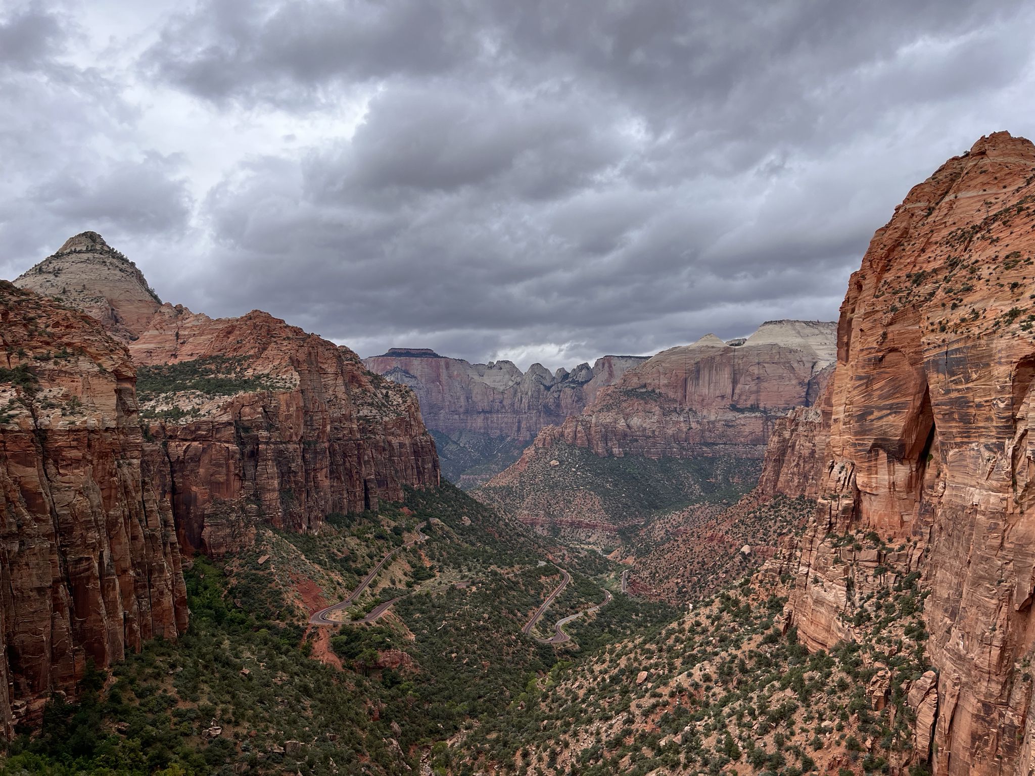 Deep canyon with towering red rock walls and green vegetation under a cloudy sky. - Tabernacle Dome & Lambs Knoll