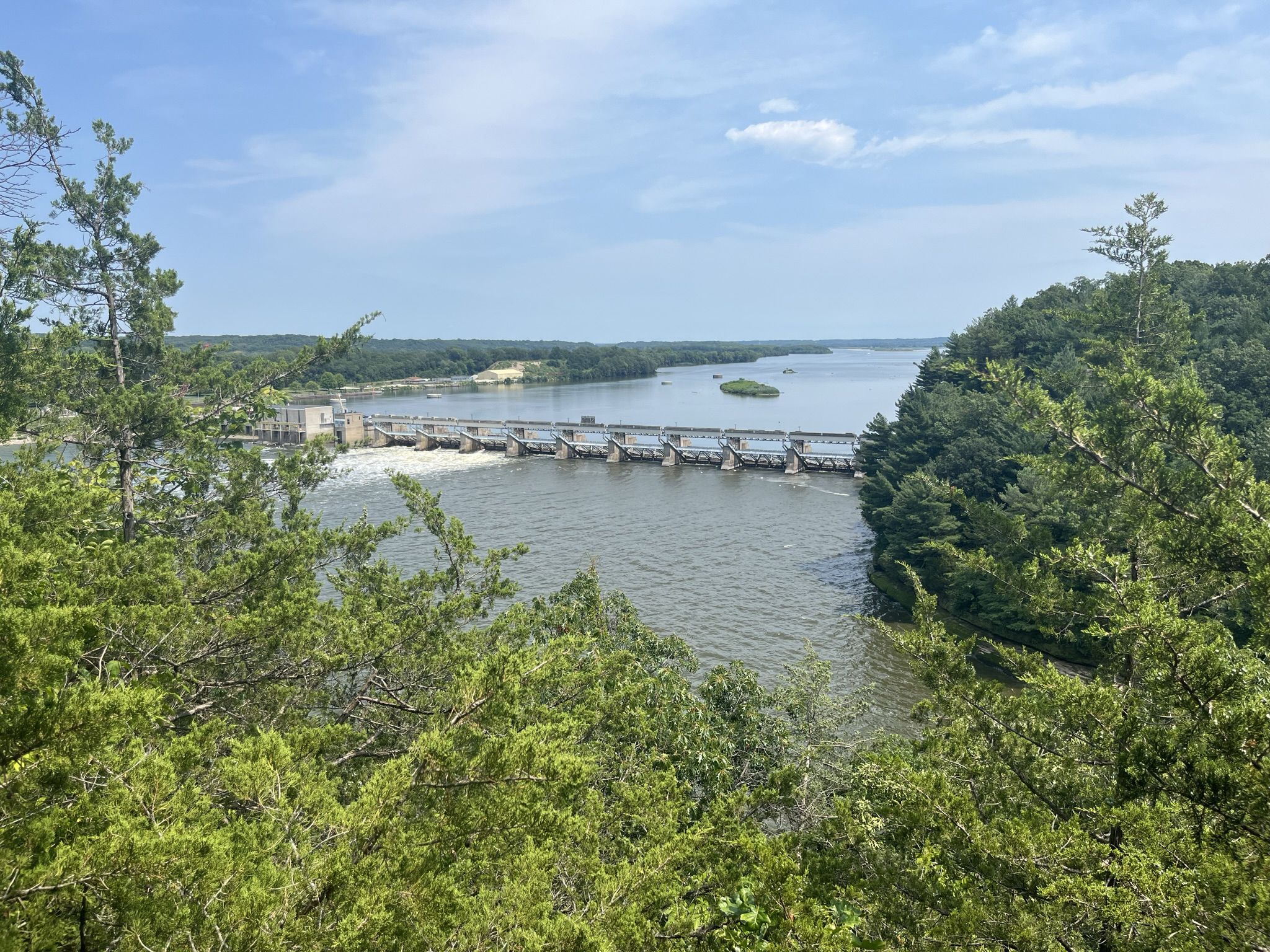 Panoramic view of a dam across a wide river, surrounded by green trees. - French Canyon