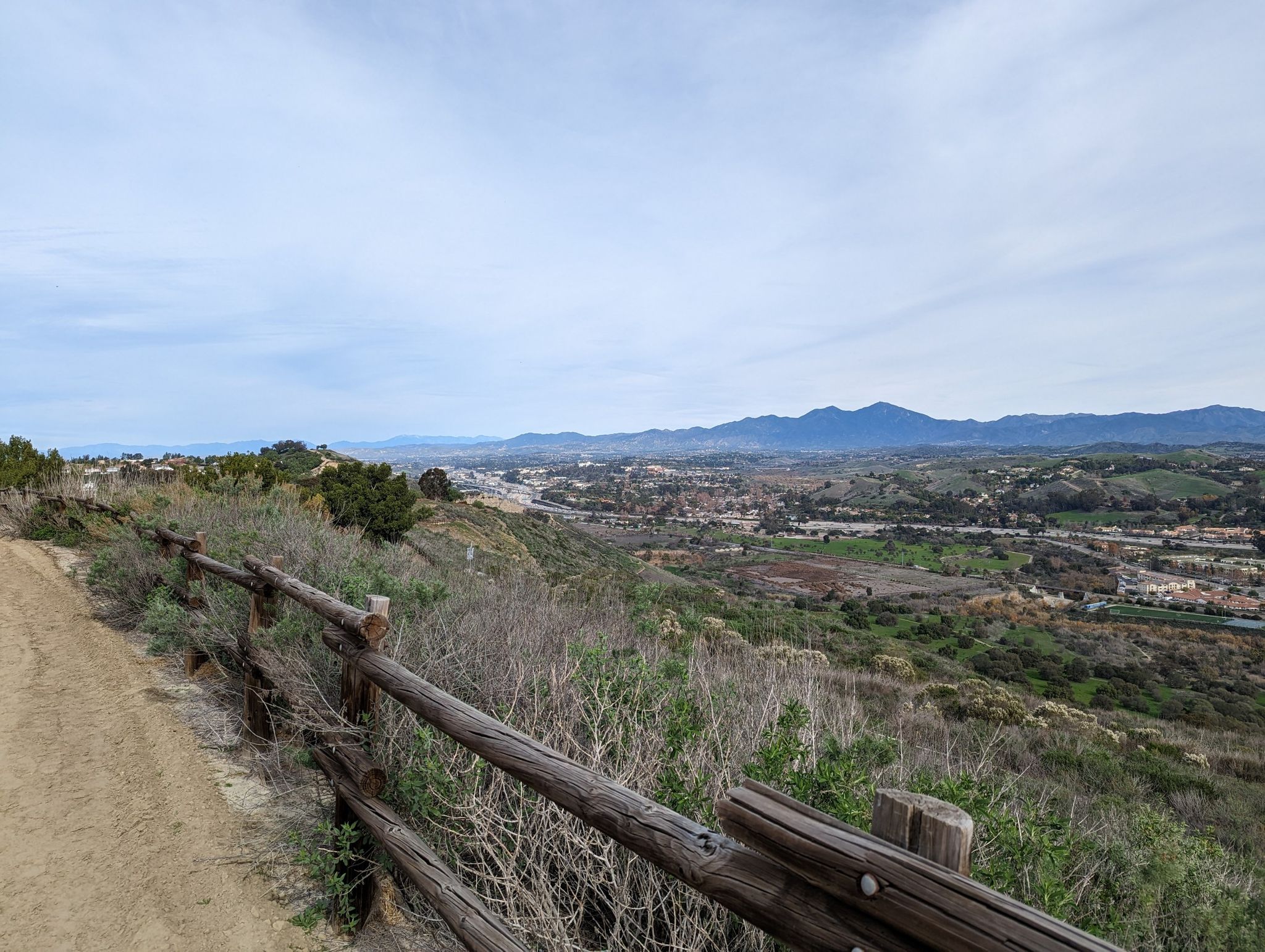Dirt path and wooden fence overlooking a distant city and mountains. - Colinas Ridge and Shea Trail Loop