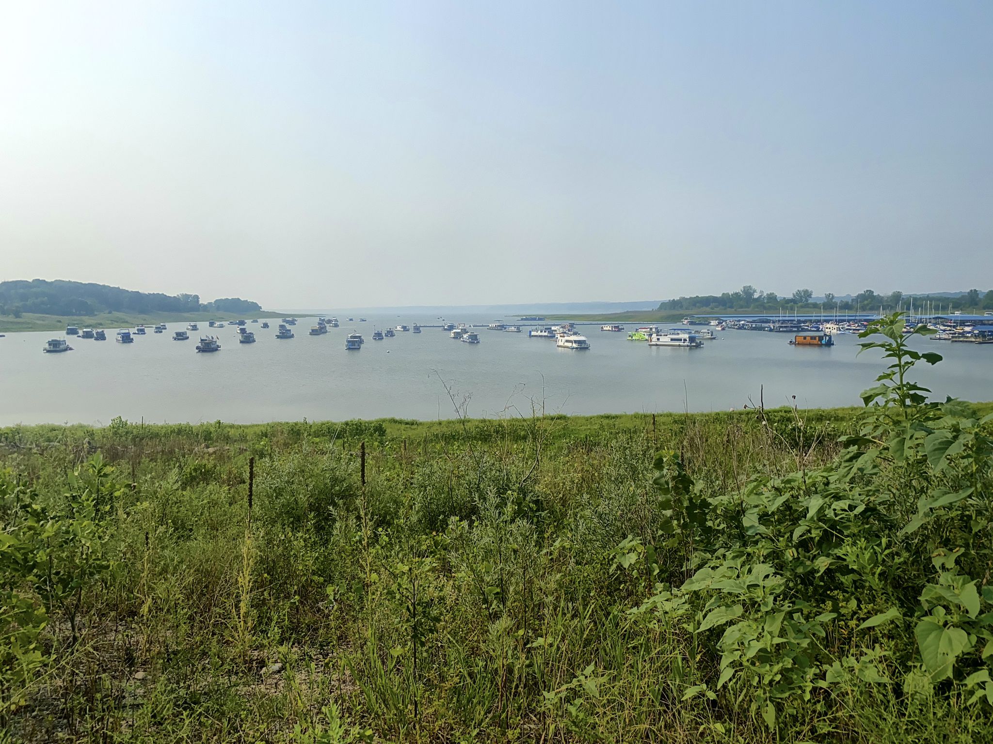 Numerous boats dot a wide, calm body of water under bright skies. - Saylorville Dam – Neal Smith Trail loop from Sycamore Wildlife Area