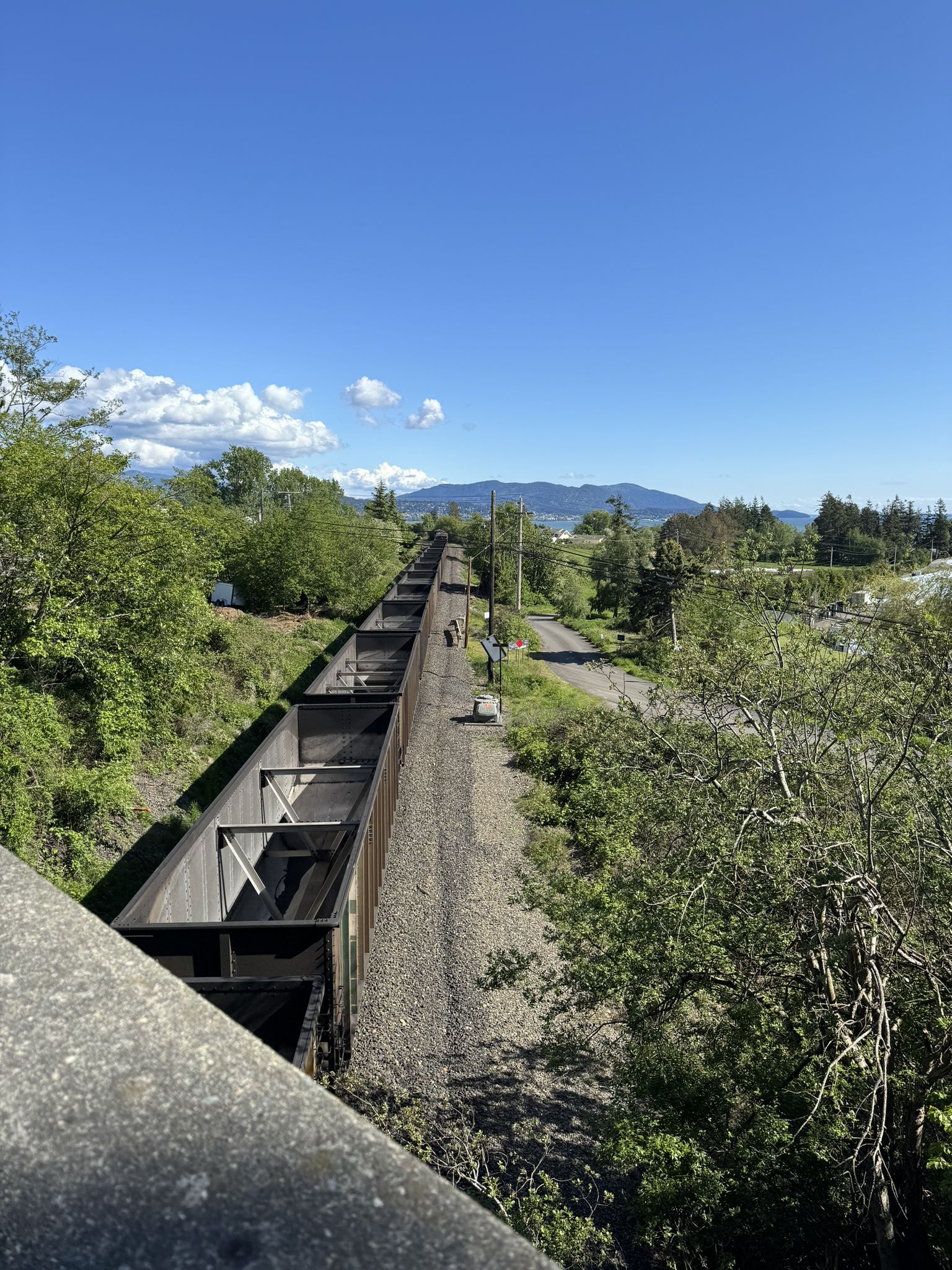 Long train cars on tracks, two people walking, under clear blue sky. - Lummi Island Overlook – Ferndale Road loop from Haxton Way at Cagey Rd