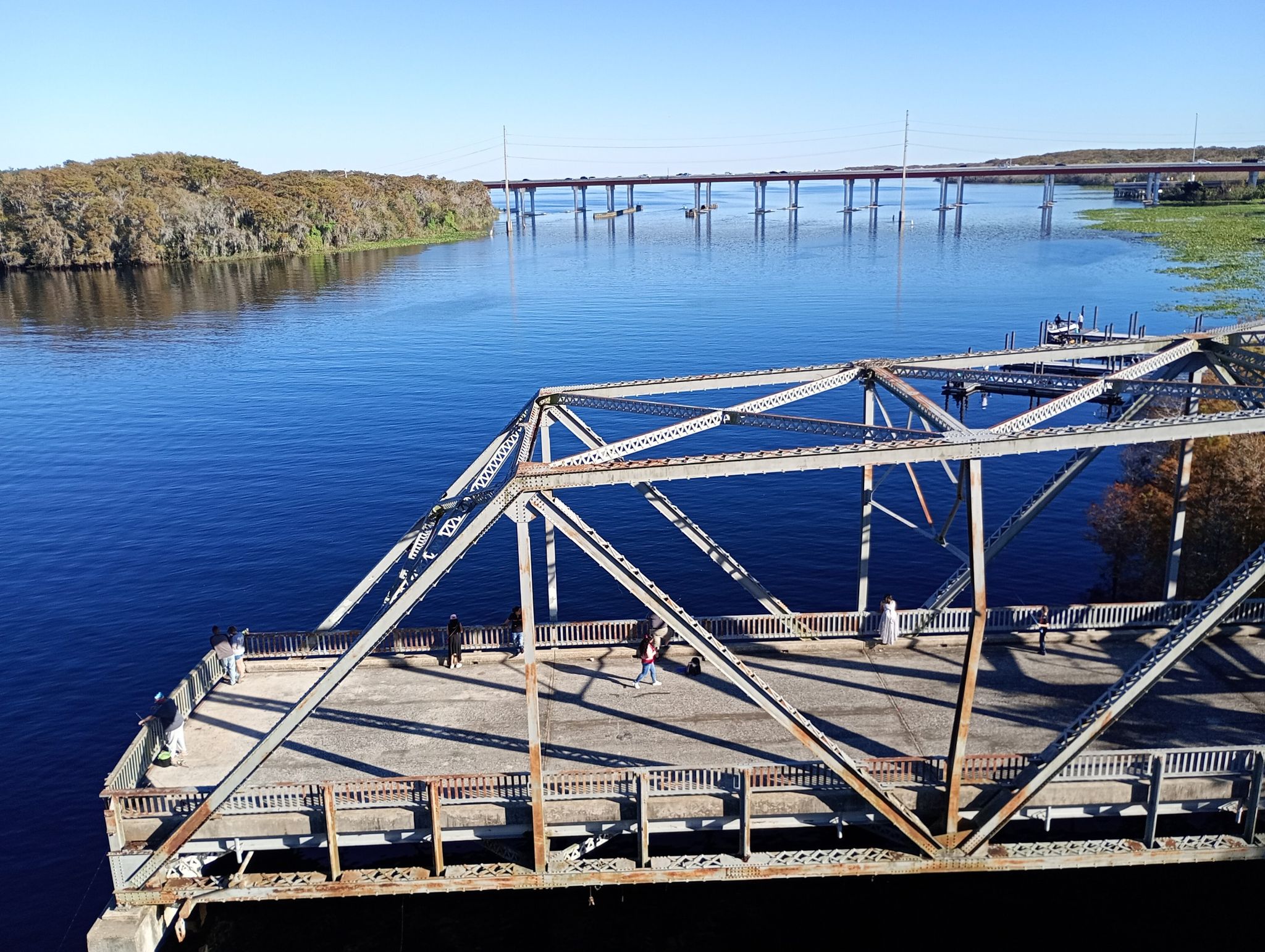 People on a metal truss bridge over a river, distant bridge visible. - Paint the Trail Artwork [Just past mile marker 7.25 EB] – Seminole Bridge loop from Altamonte Springs