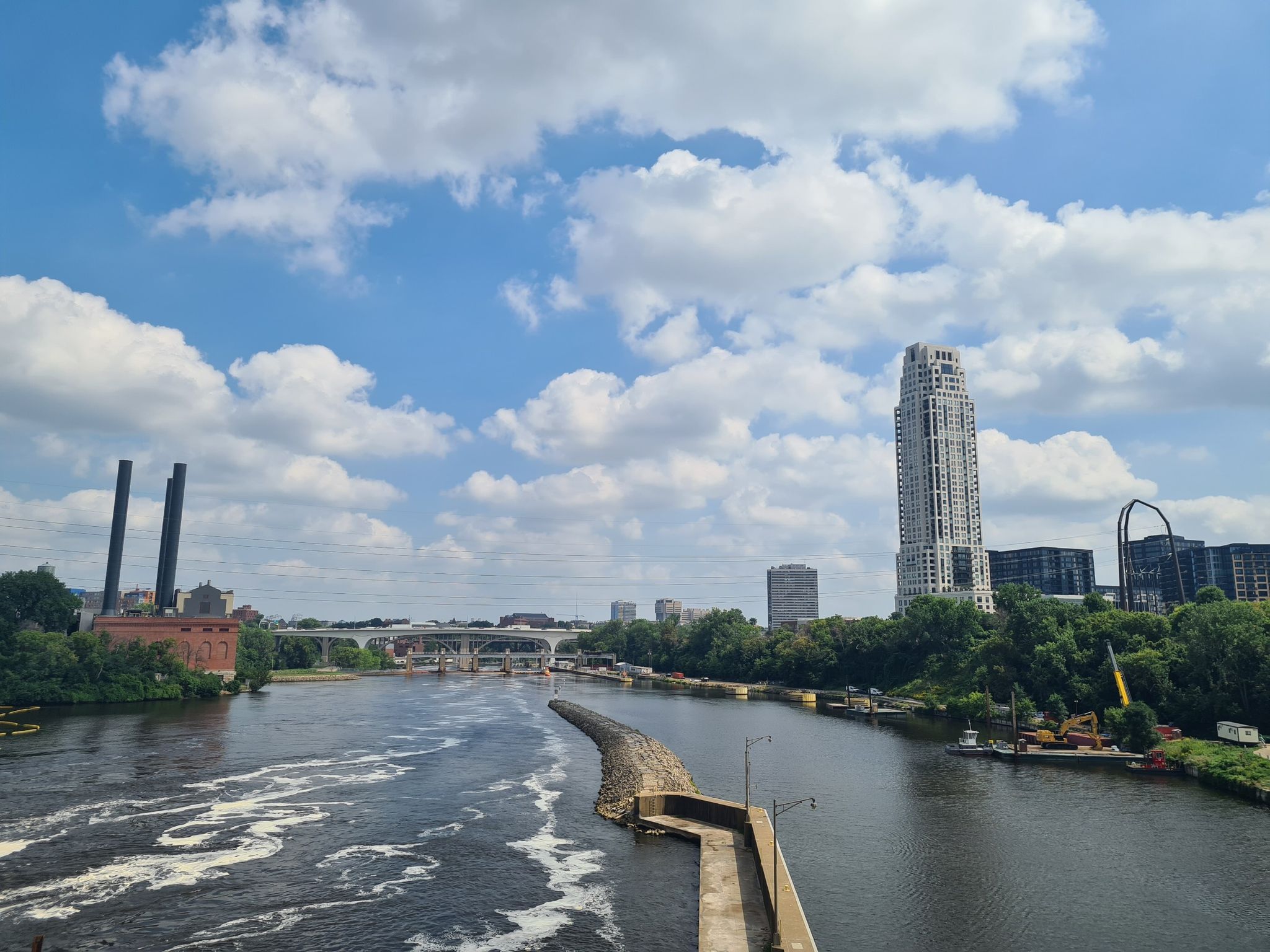 Wide river with foamy water, city skyline, and industrial buildings under a cloudy sky. - Stone Arch Bridge loop from Mississippi River