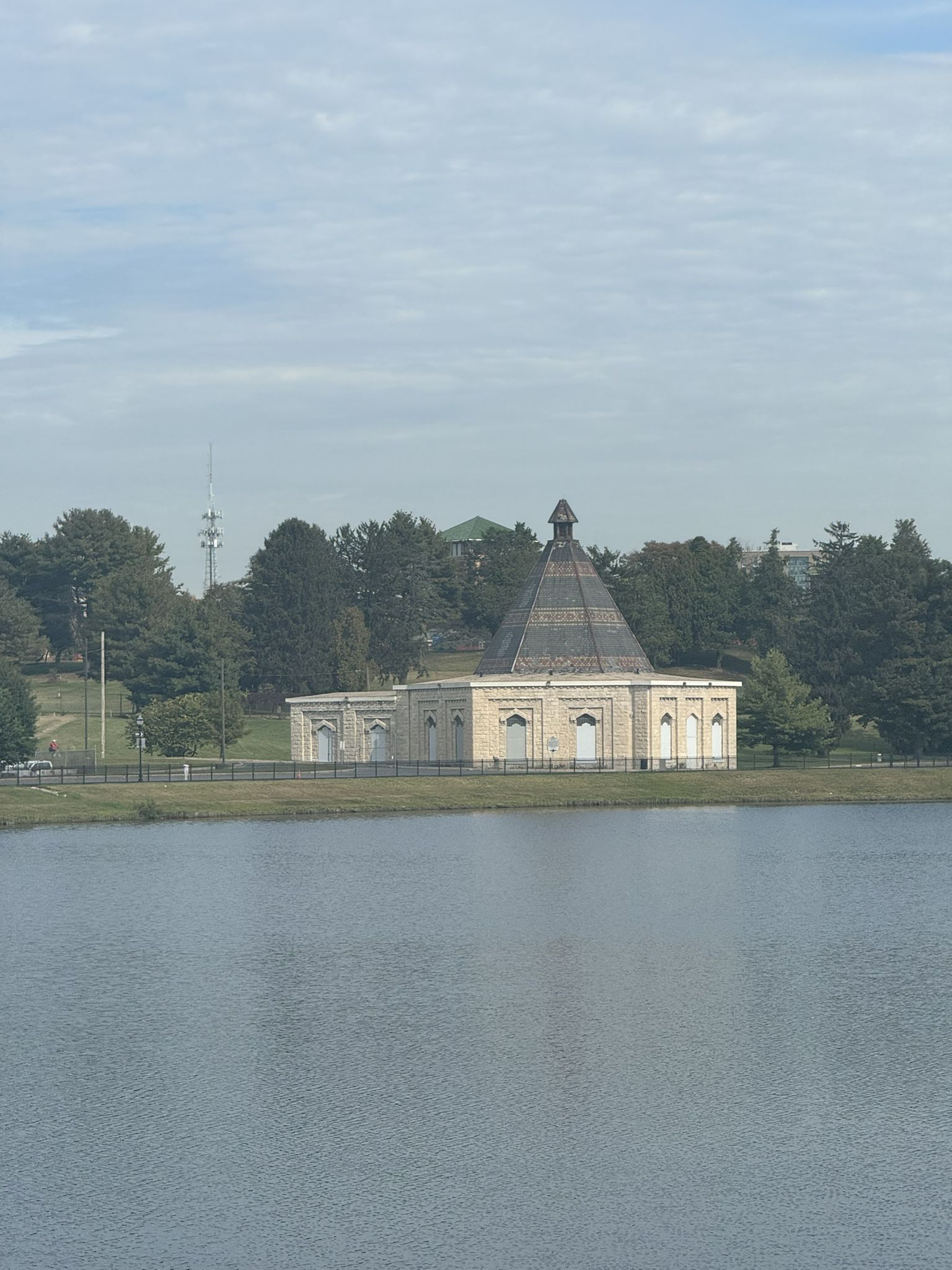 Unique building with dark roof by water, surrounded by trees under overcast sky. - Lake Montebello and Herring Run Trail