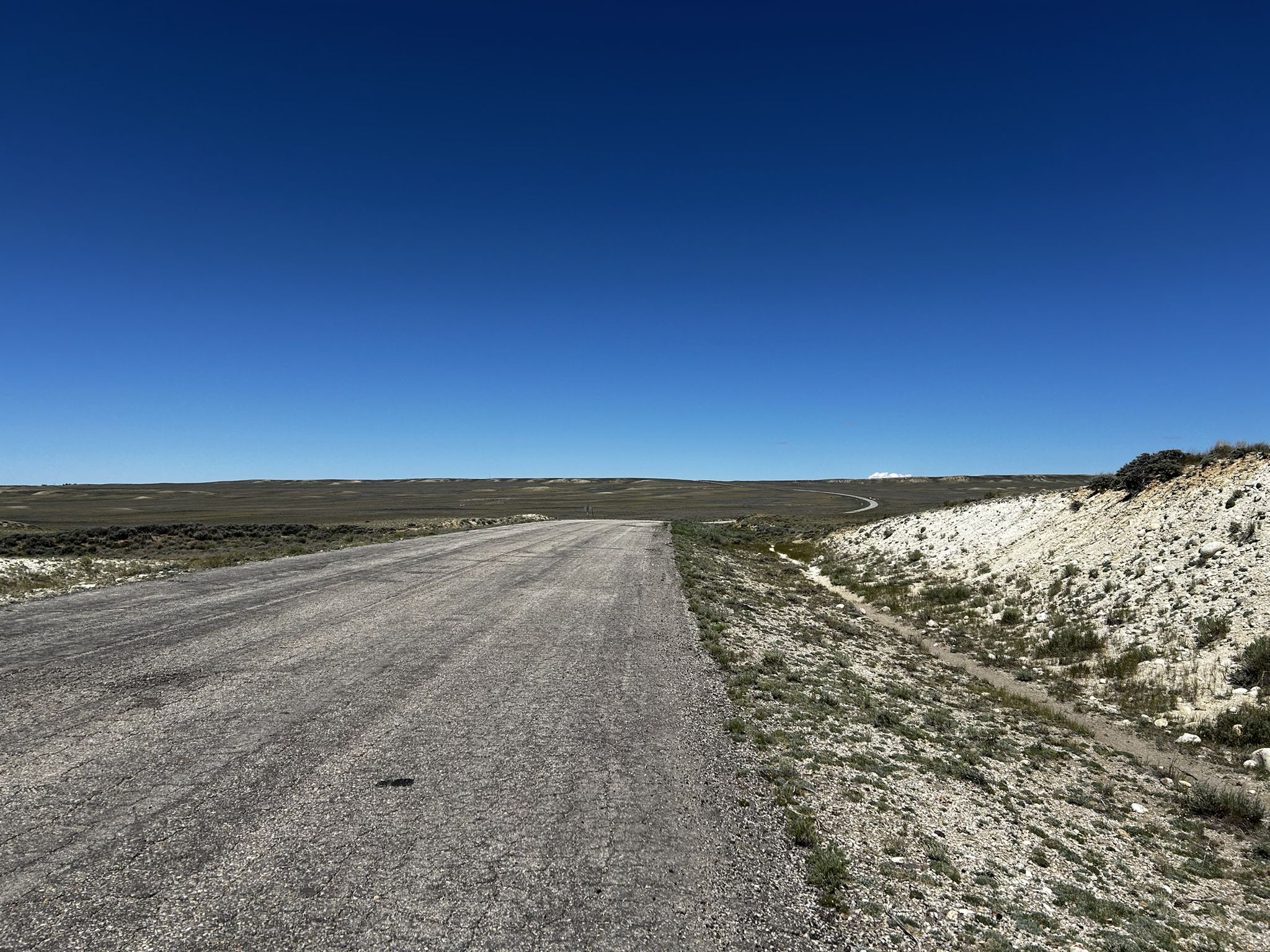 A long dirt road cuts through a flat, arid landscape under a clear sky. - Rawlins Walking Tour loop
