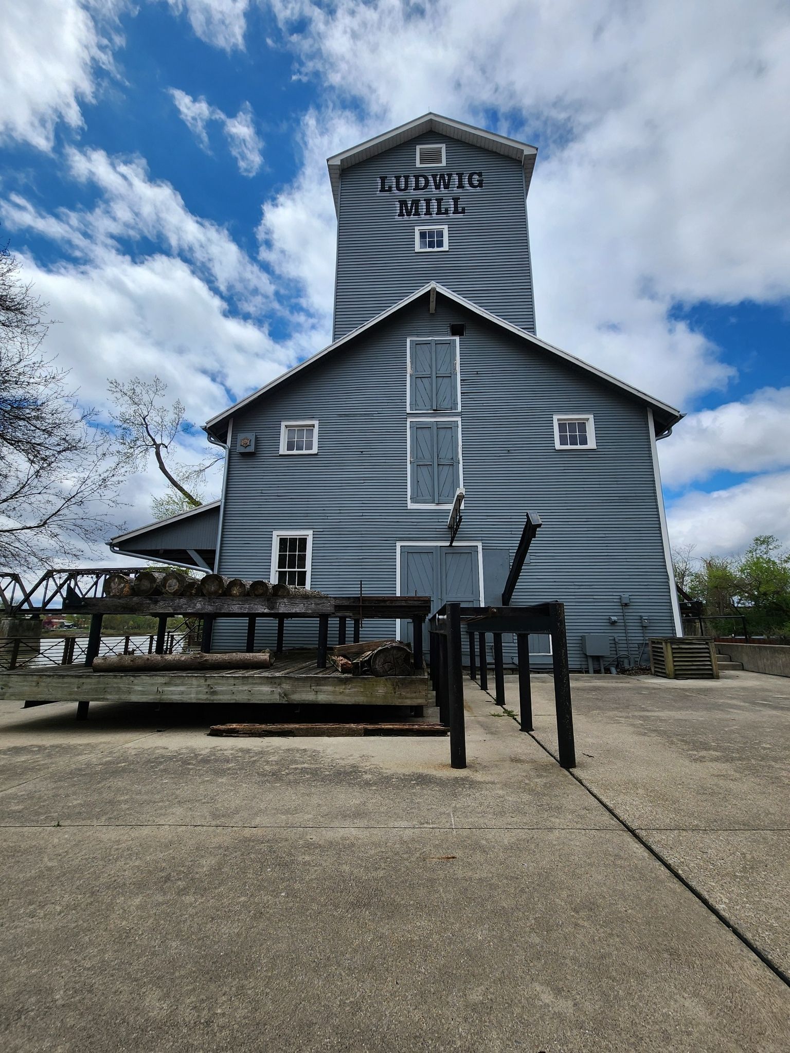 A tall grey mill building stands under a bright blue cloudy sky. - Isaac Ludwig Mill loop from Grand Rapids