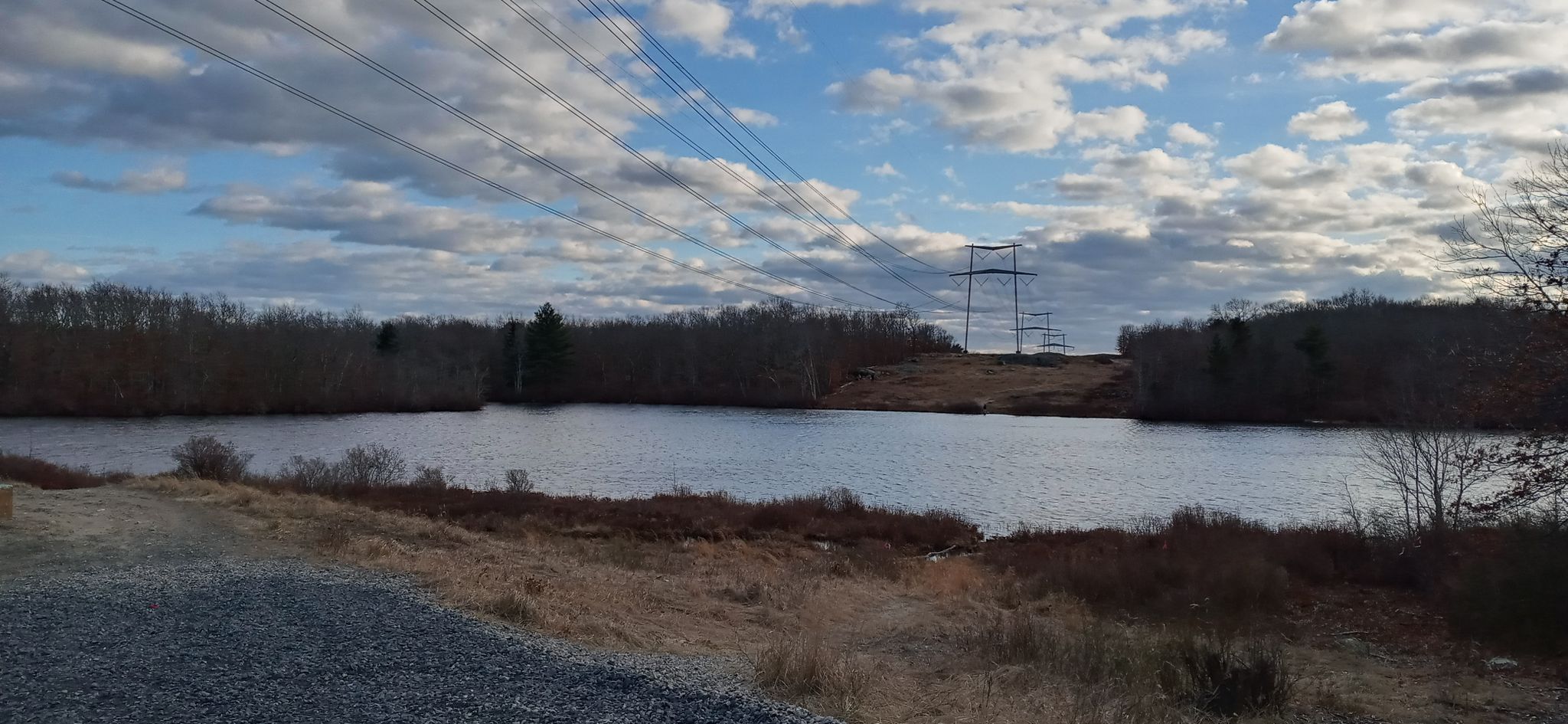 Calm lake with bare trees, power lines, and cloudy blue sky. - Witch Trail Loop