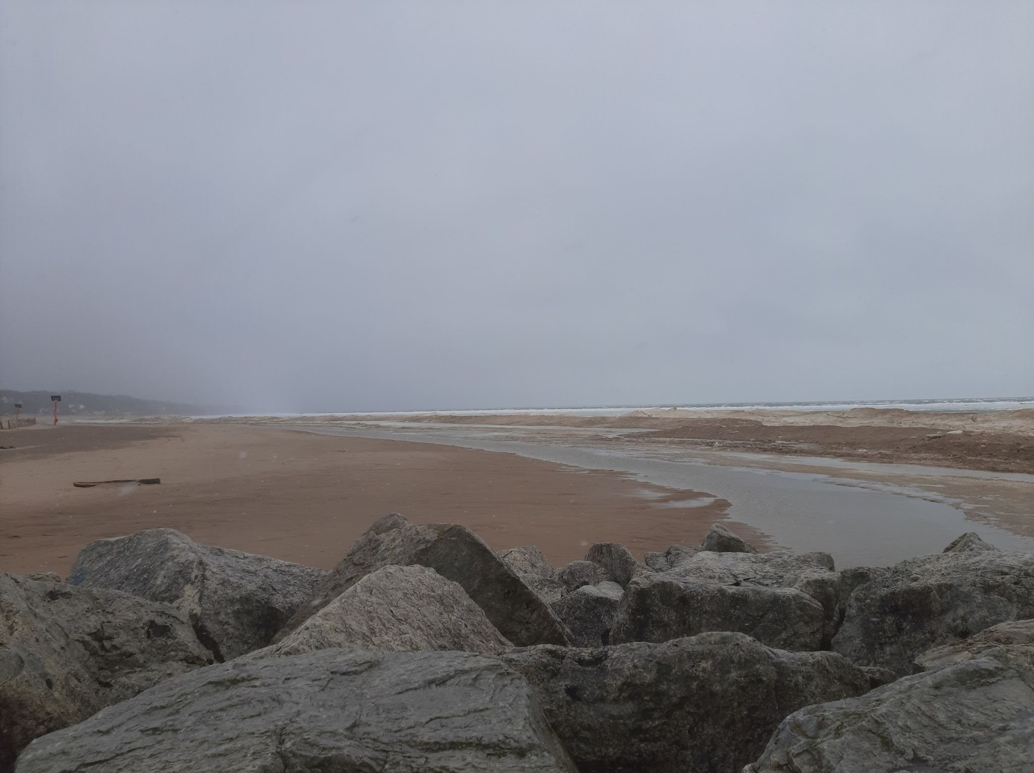 Large rocks, wide sandy beach, and calm water under a gray sky. - Grand Haven City Beach – Grand Haven State Park loop from Grand Haven Charter Township