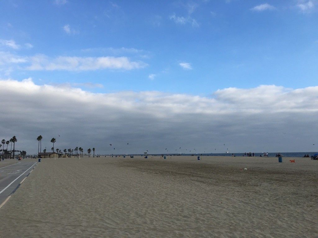 Wide sandy beach with distant people and palm trees under a cloudy sky. - Naples Island loop