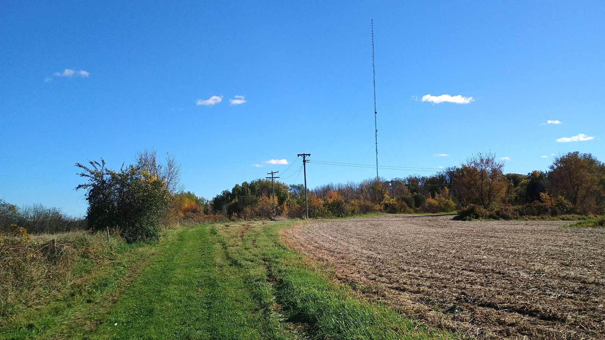 Grassy path next to a tilled field, with a tall tower under a blue sky. - Complex trail junction – Lone Rock Trailhead loop from Vermillion Highlands Research Recreation and Wildlife Management Area