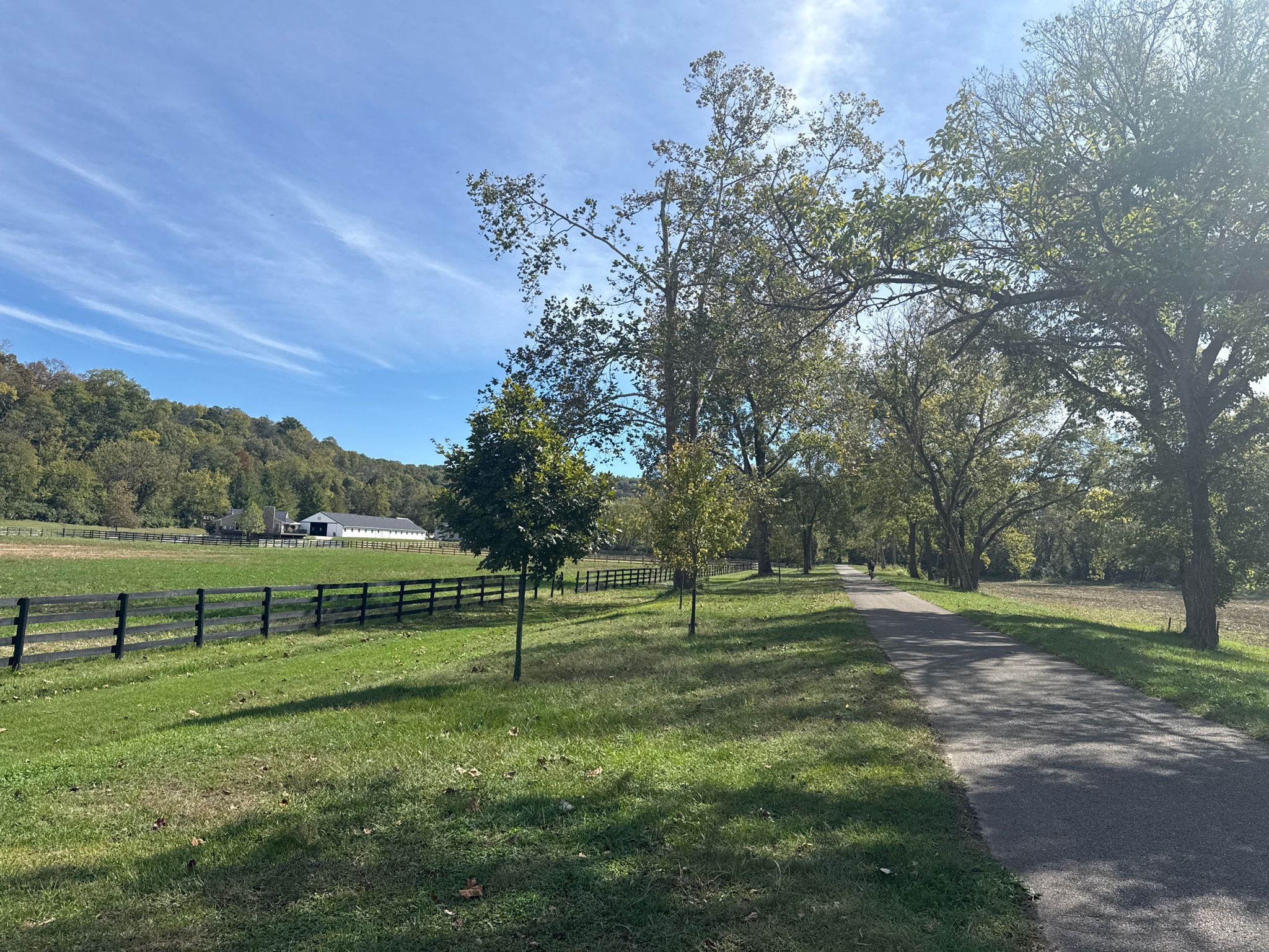 A sunny paved path runs beside a fenced field with trees and distant hills. - Little Miami Scenic Trail: Caesar Creek Gorge to Oregonia