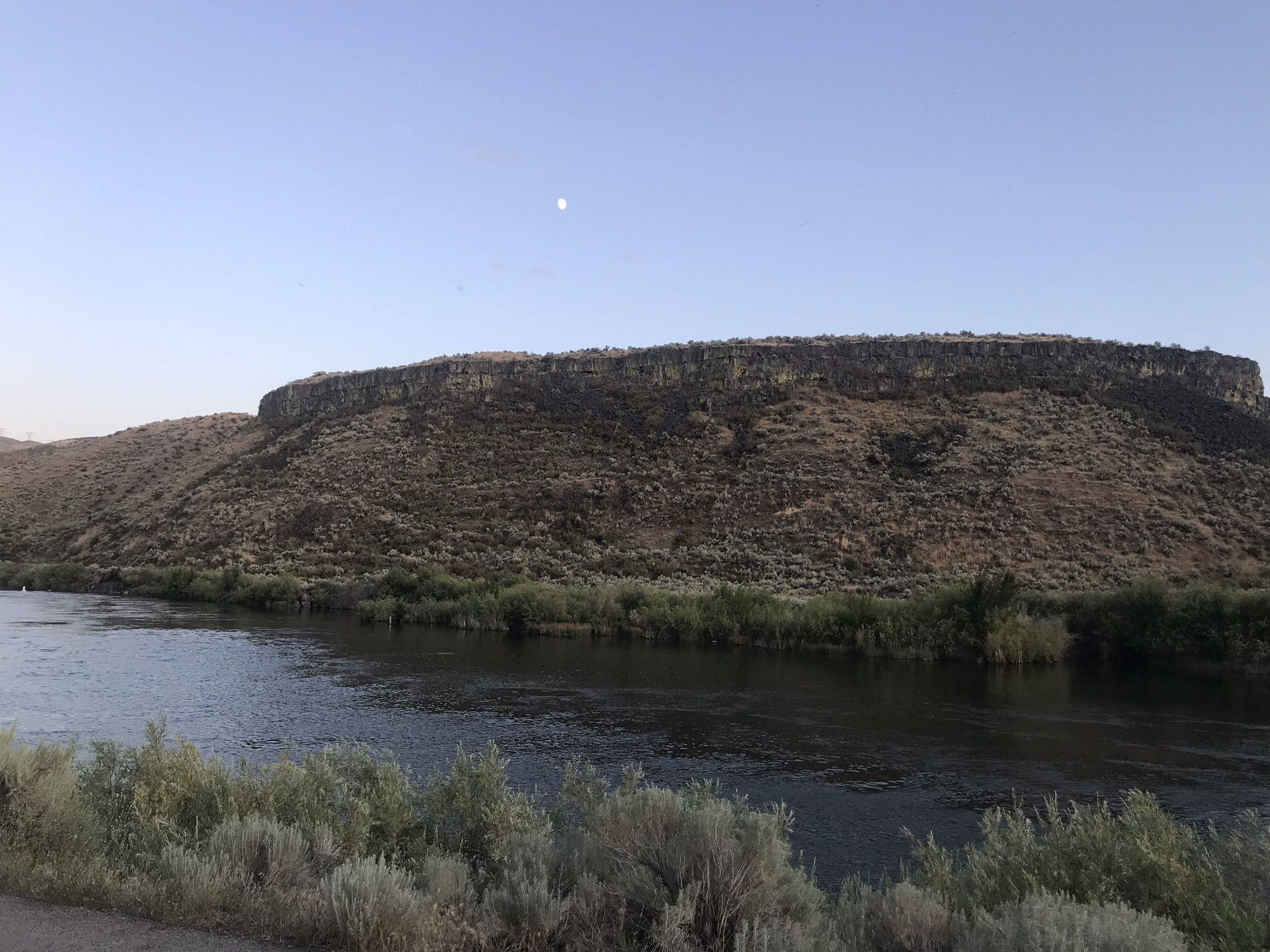A wide river flows past a large, dark, flat-topped hill under a clear sky. - Boise River – Boise River Greenbelt loop from Golda Harris Nature Preserve