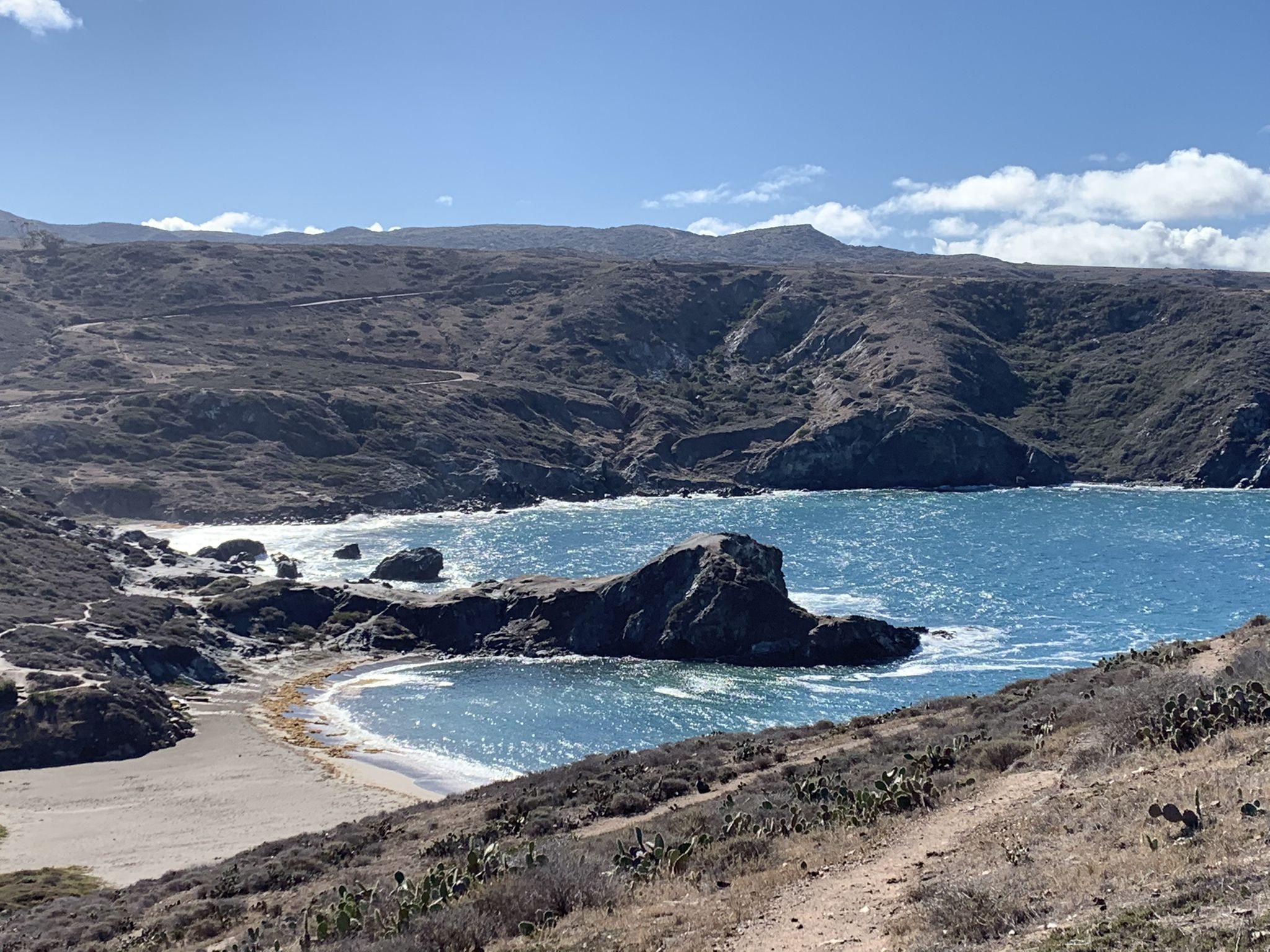 Rocky cove with turquoise water, sandy beach, and a prominent rock formation. - Trans-Catalina Trail: Little Harbor to Two Harbors