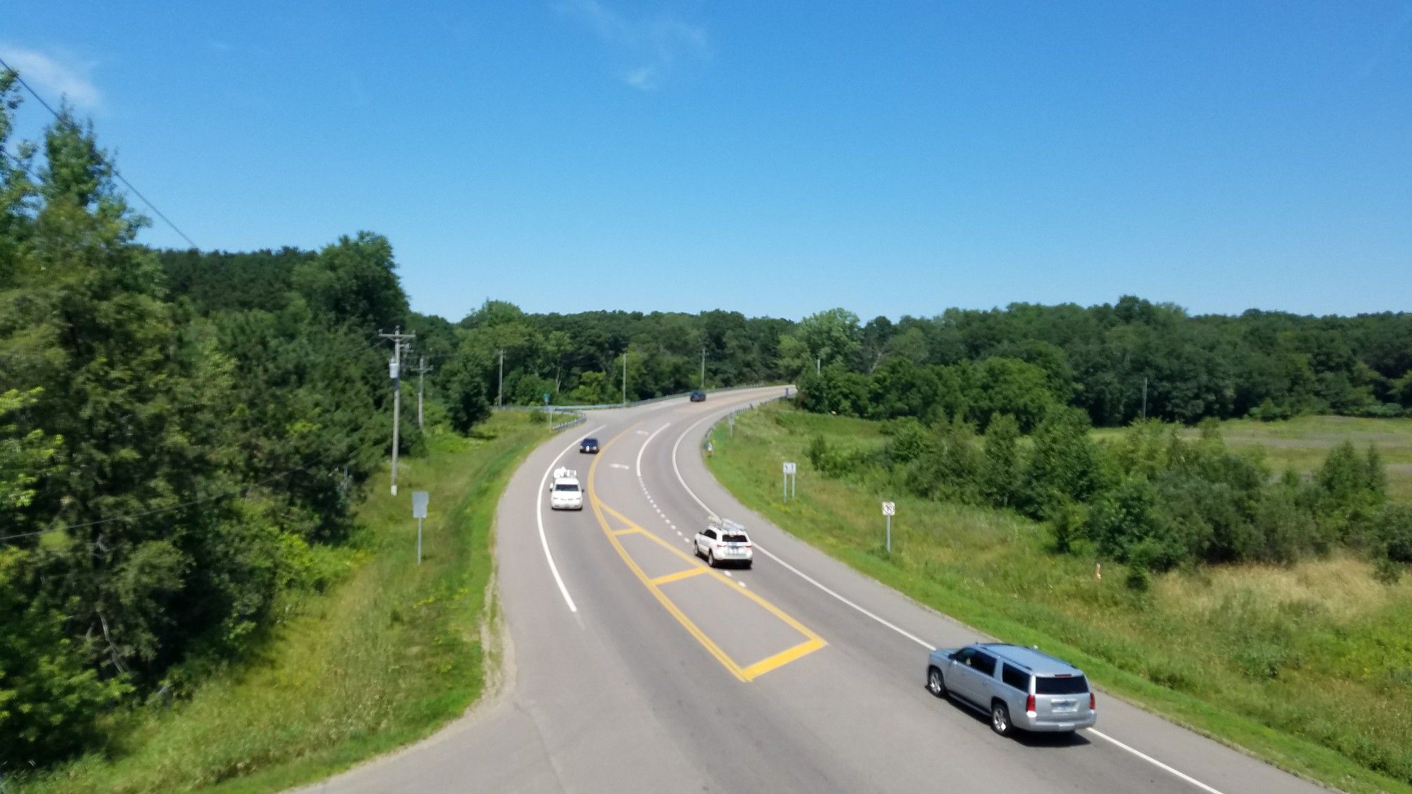 Cars driving on a winding highway through green trees under a blue sky. - Duluth Junction – Bavarian Hunter Restaurant loop from Grill Stand
