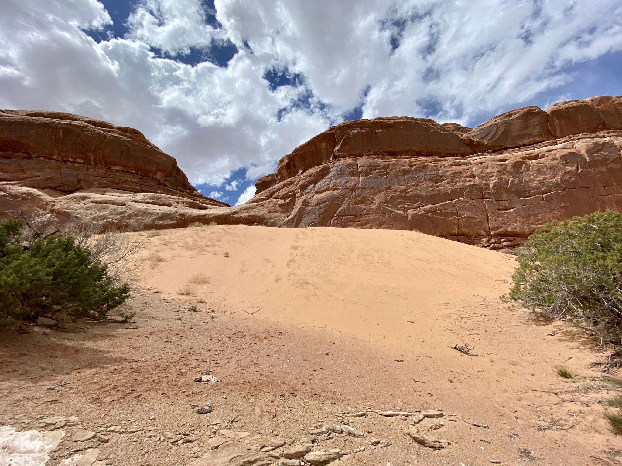 A sandy dune nestled between large red rock formations under a cloudy sky. - Lower Monitor & Merrimac Trail Loop