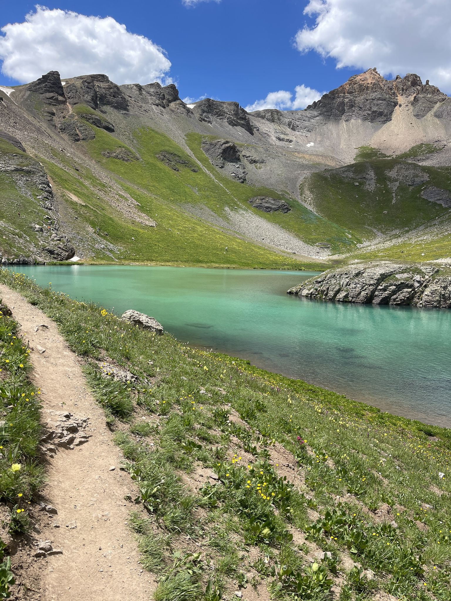 Dirt trail alongside a vibrant turquoise lake, green mountains under a blue sky. - Ice Lake Trailhead – Clear Creek Waterfall loop from Ice Lakes Trailhead Parking