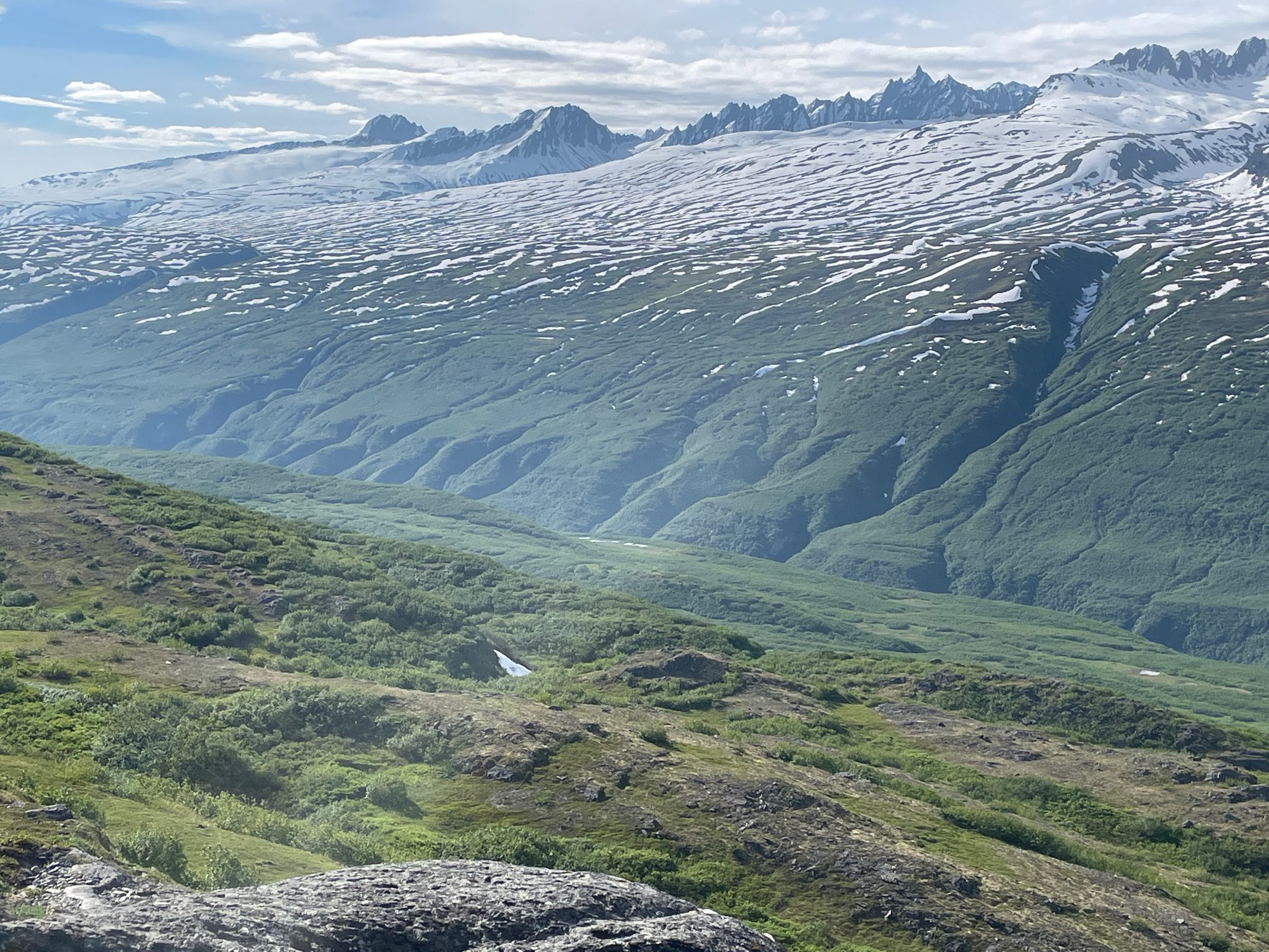 Vast mountain landscape with snow-capped peaks, green valleys, and a small white tent. - Thompson Pass Pack Trail