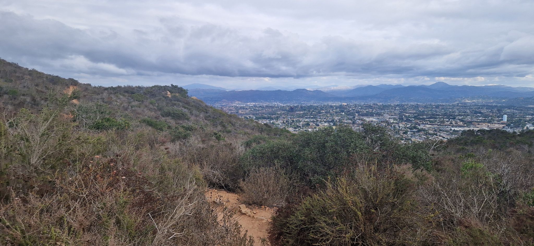 Overcast view of a distant city from a brush-covered hillside. - Pyles Peak Trail via Barker Way