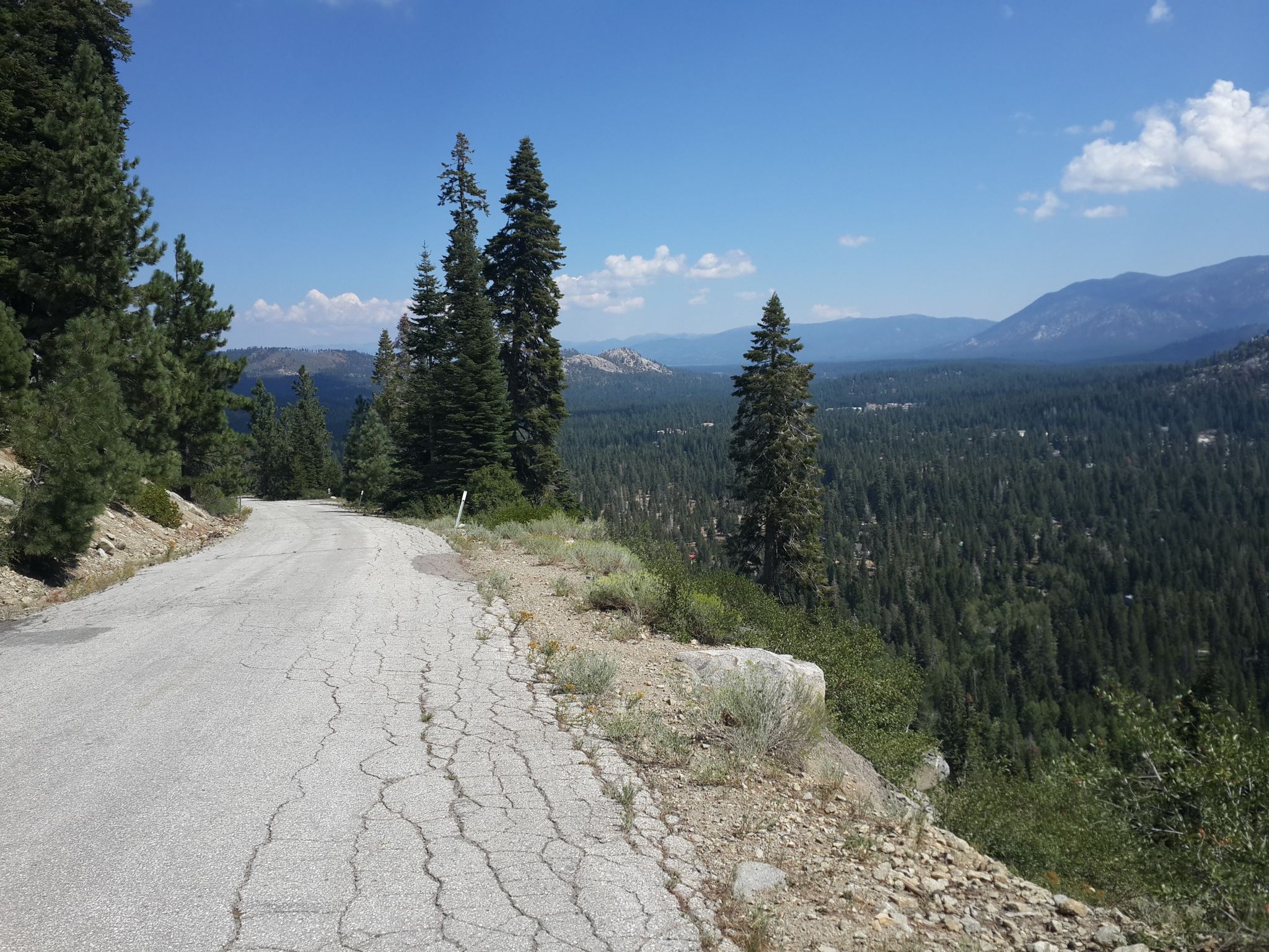 Cracked paved road overlooking a vast forest and distant mountains on a sunny day. - Old Meyers Grade to Echo Summit