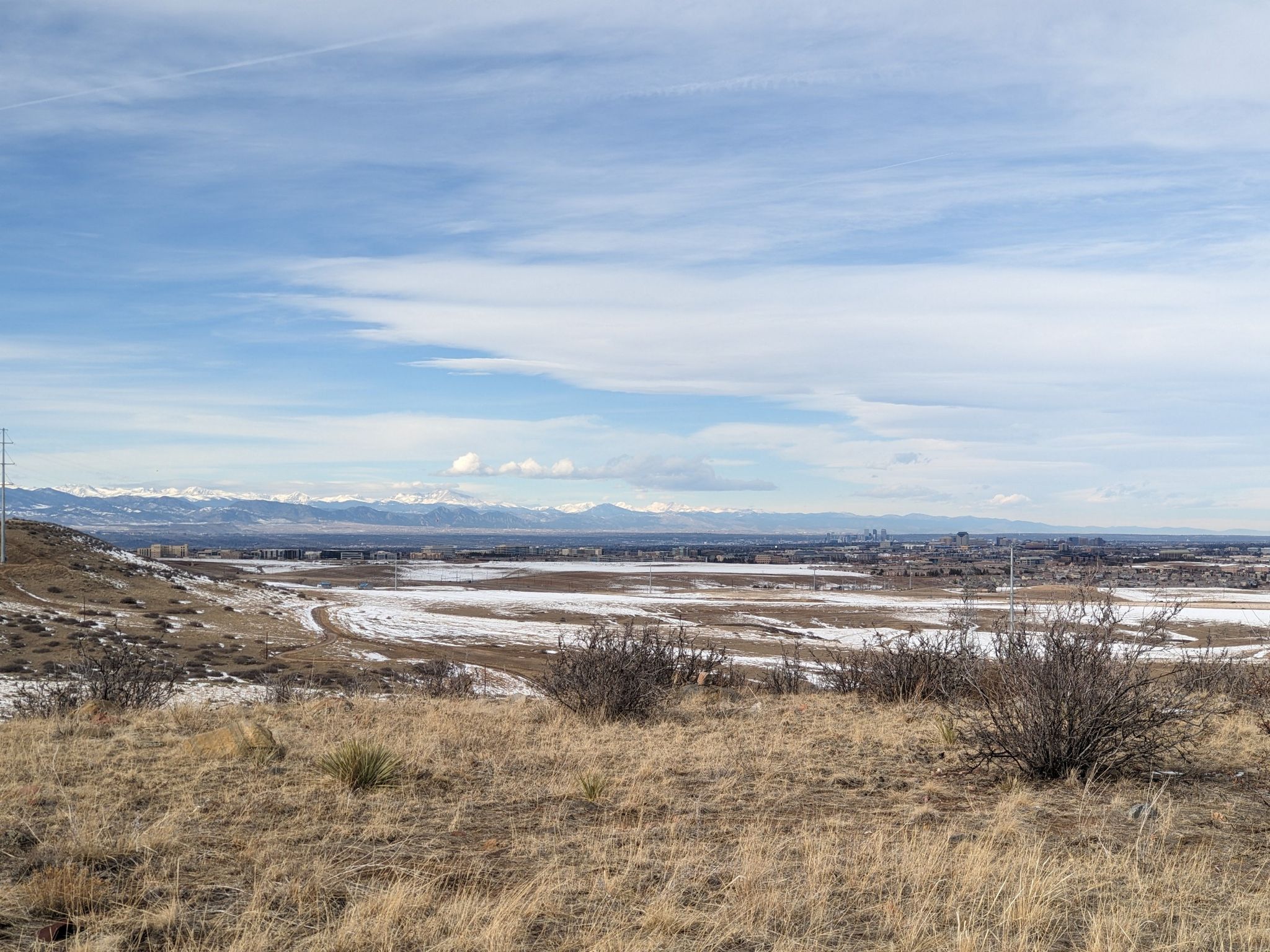 Expansive winter landscape with dry grass, snow-dusted fields, and distant mountains under a bright sky. - Rosie Rueter Trail Loop
