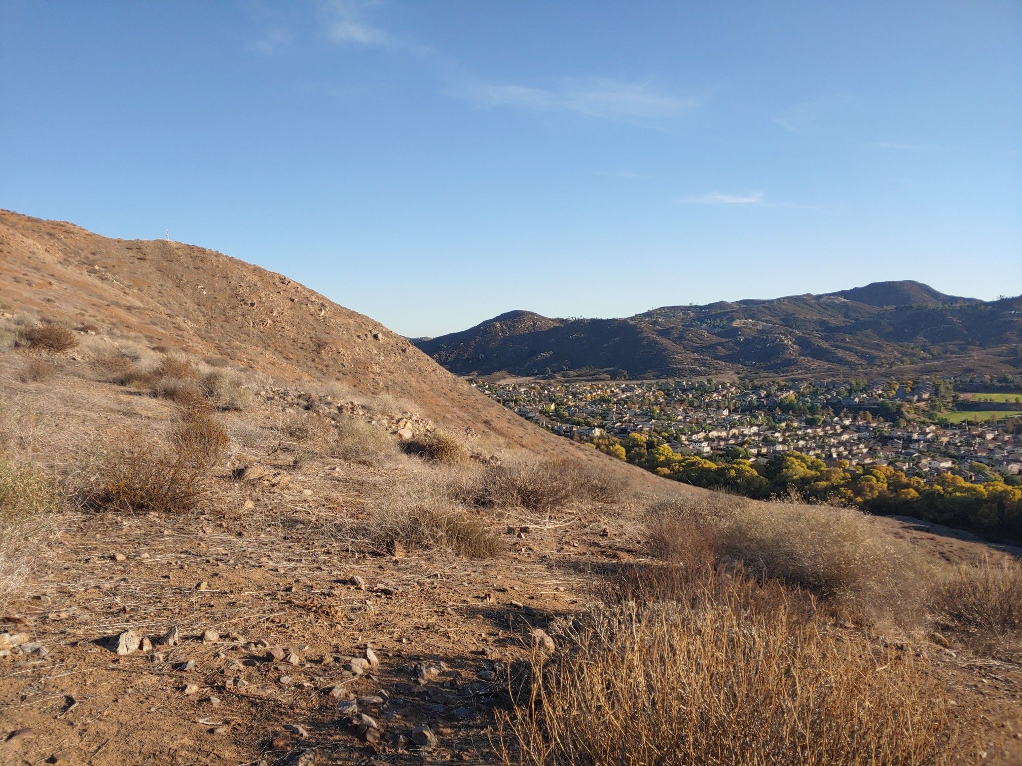 Dry, rocky hillside overlooking a green valley with a town and distant mountains. - Creek to Flag Trail