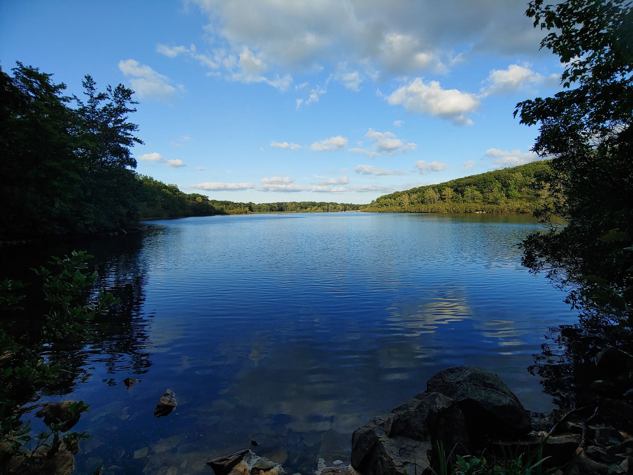 Calm lake reflecting blue sky and clouds, surrounded by green hills. - Breakneck Mountain and Panther Mountain Loop