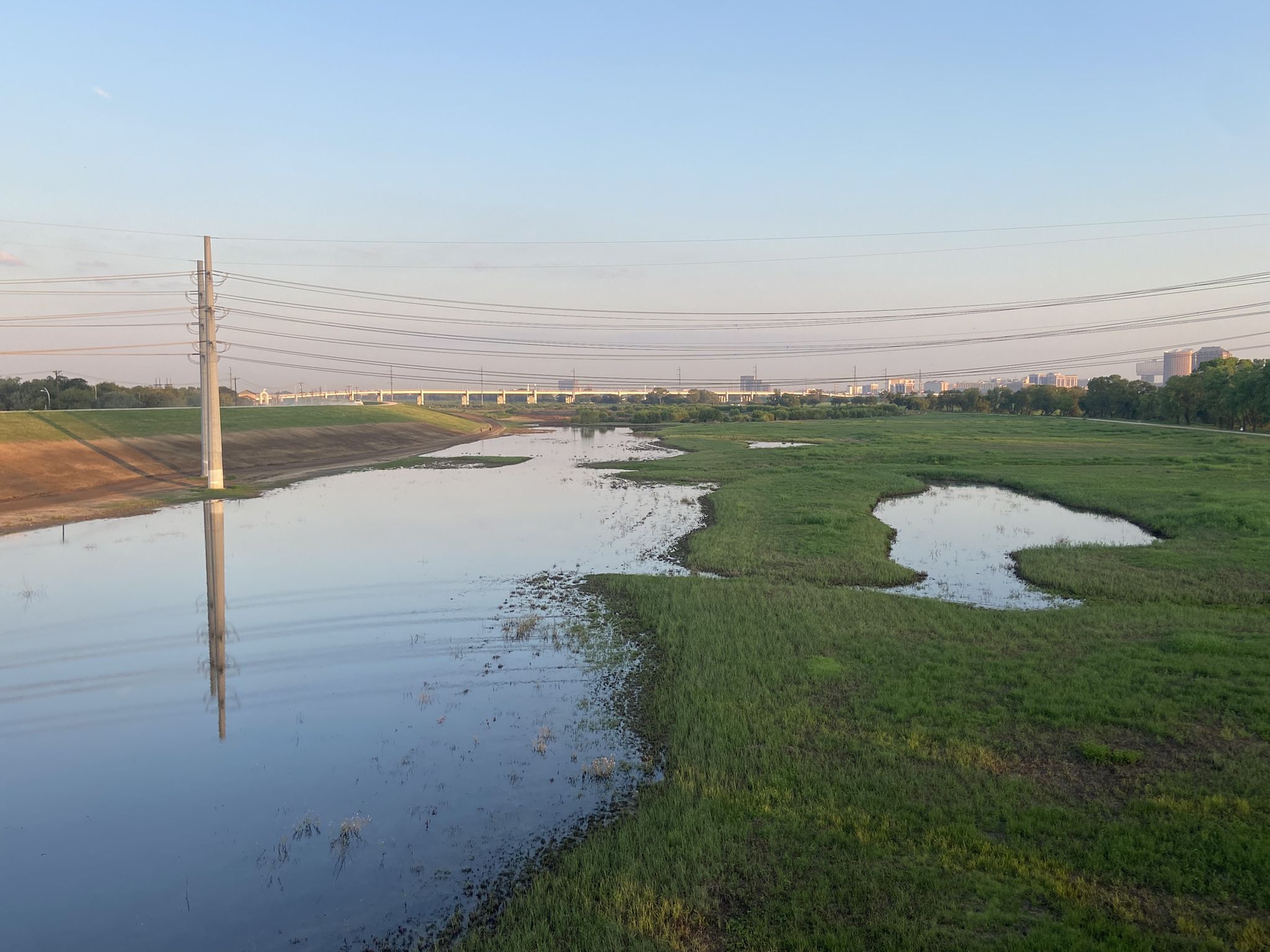 River flowing through green fields under power lines on a clear day. - The Loop and White Rock Lake Trail