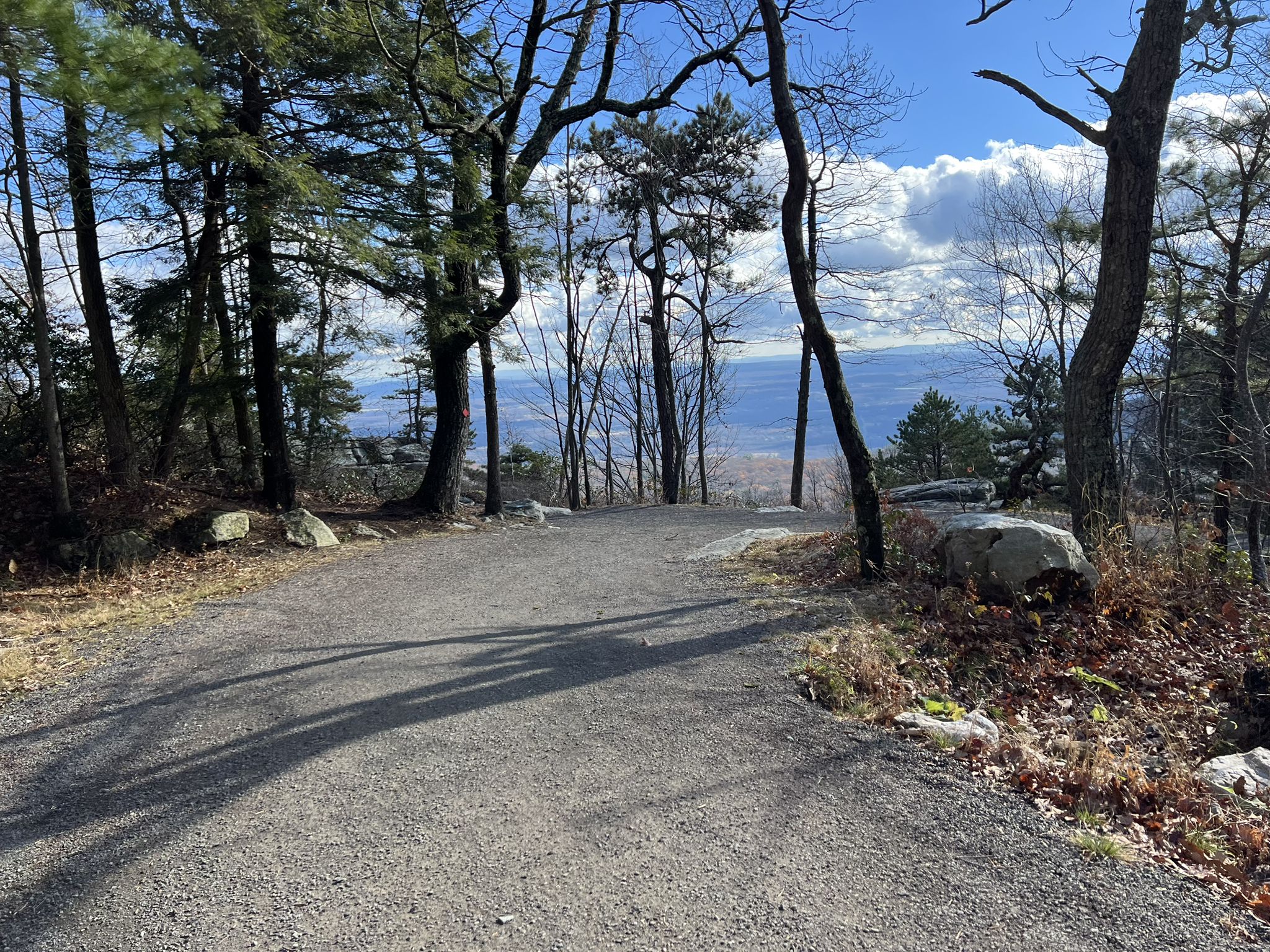 A gravel path through trees overlooking a distant valley under a cloudy sky. - Gertrude's Nose and Millbrook Mountain Loop