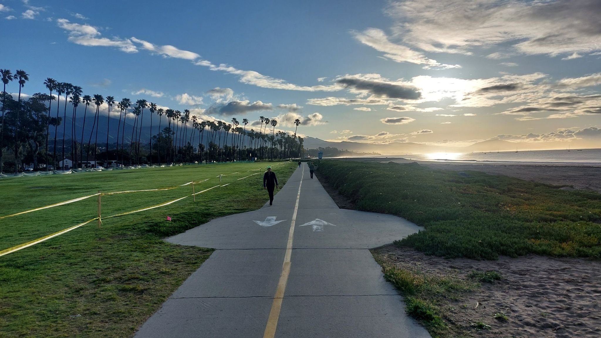 Paved path with people walking, palm trees, and sunset over the ocean. - Stearns Wharf – East Beach loop from Santa Barbara