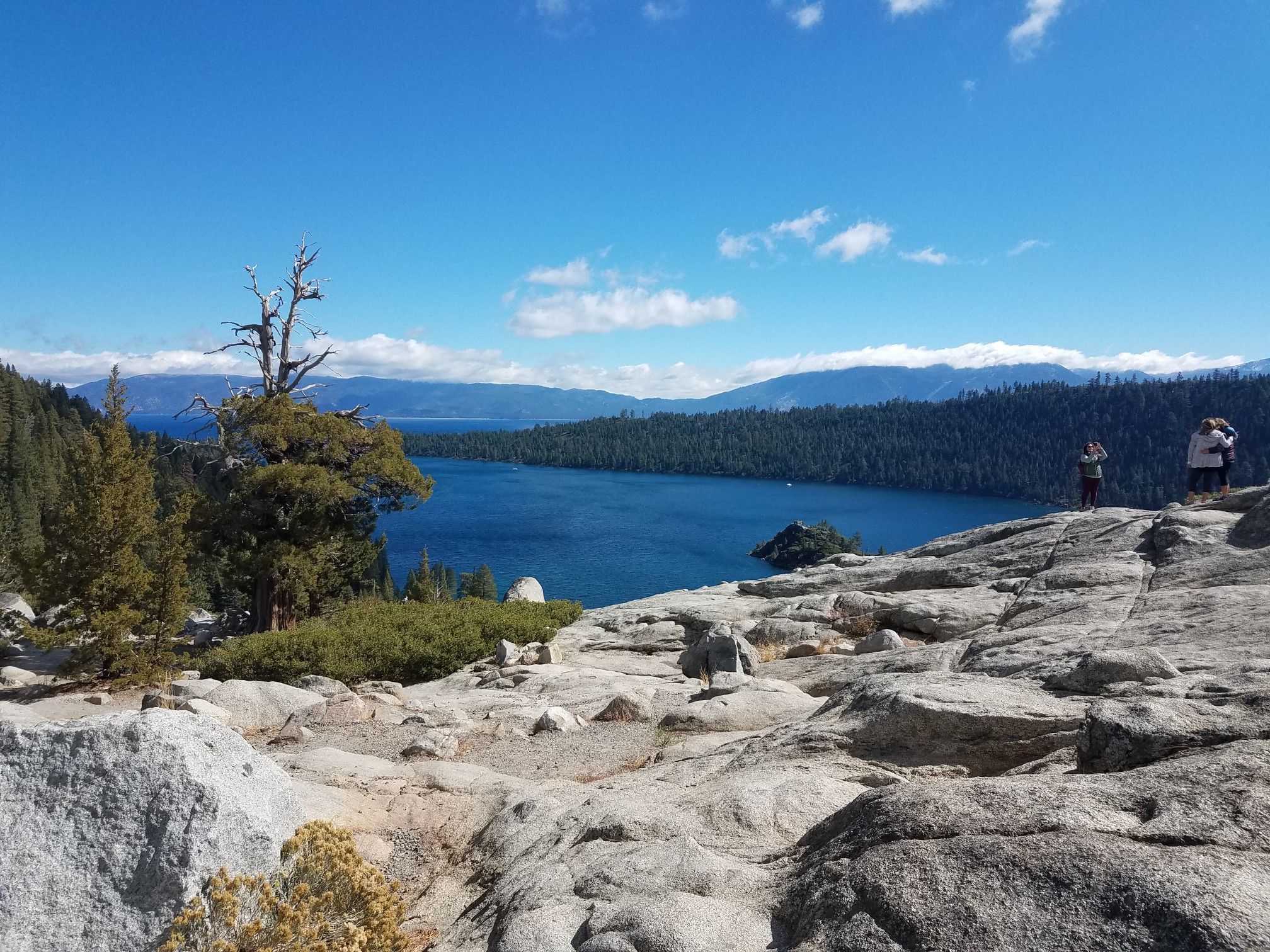 Two people on rocky outcrop overlooking a large blue lake and distant mountains. - Emerald Bay Road to Vikingsholm Trail loop