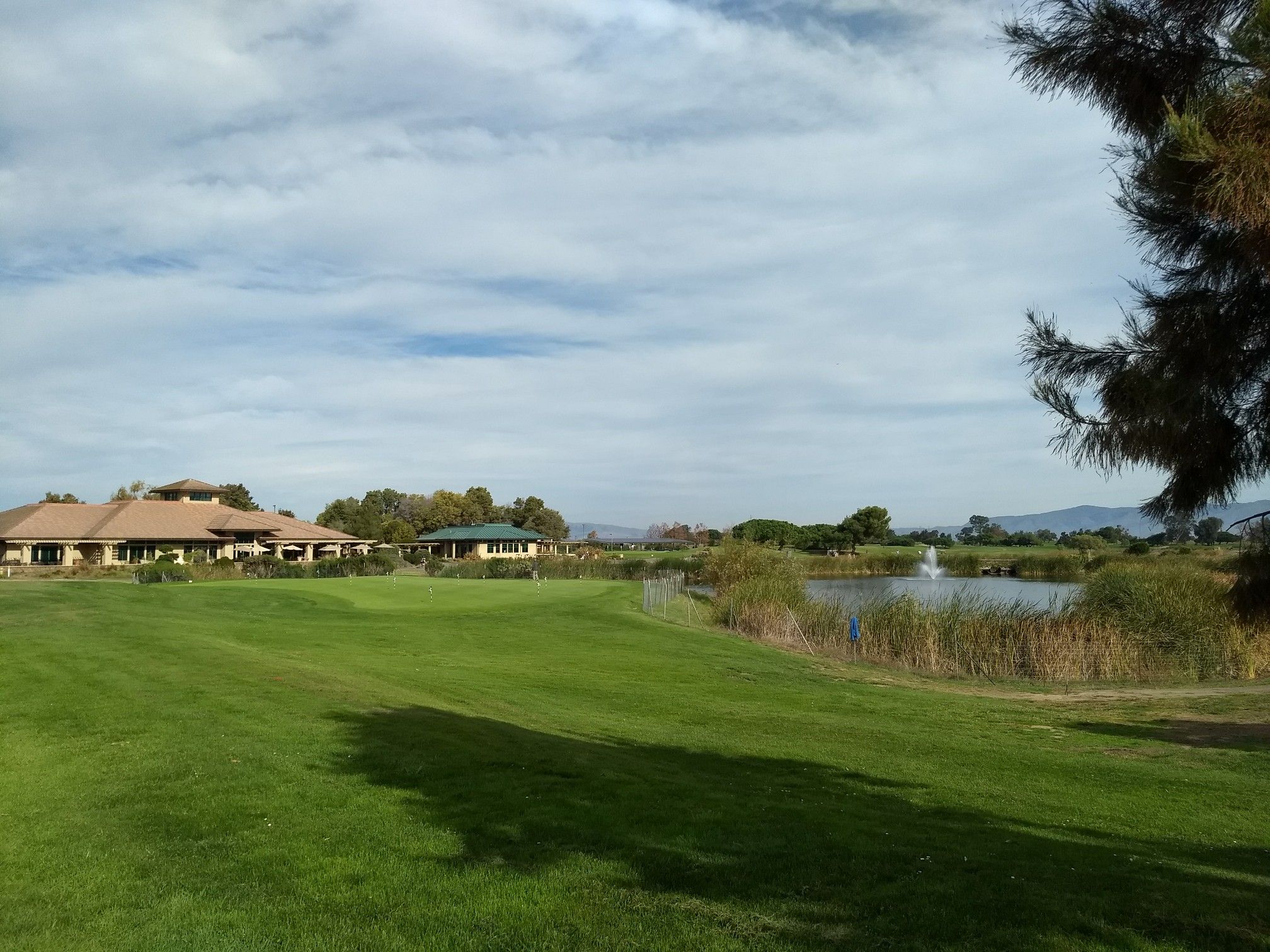 Green golf course with buildings, a pond, and a fountain under a cloudy sky. - Permanente Creek and Vista Slope Trail