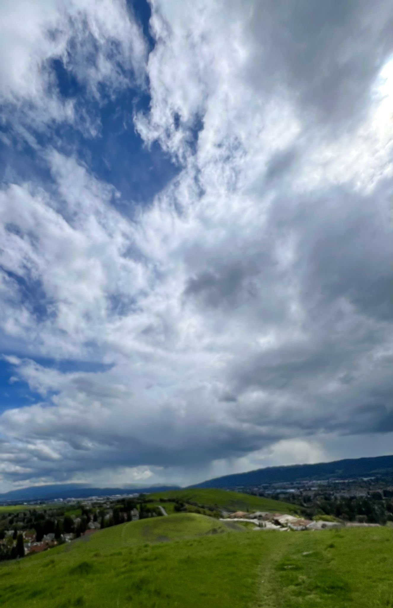 Vast green rolling hills under a dramatic cloudy sky, with a distant town. - Dougherty Valley Ridge Trail