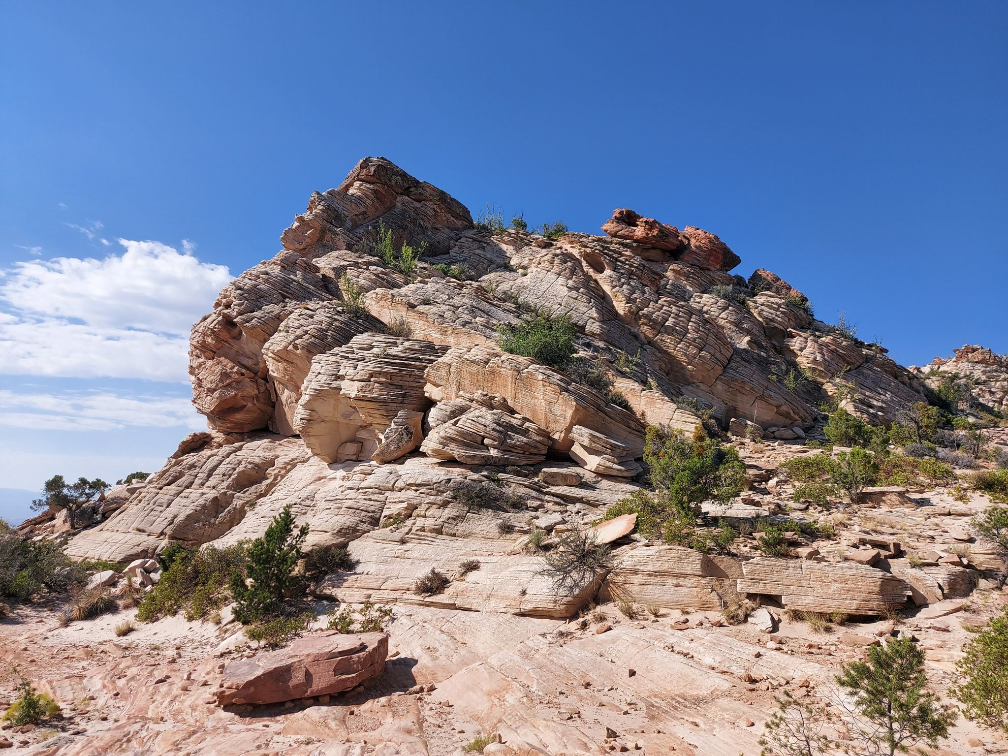 Large, layered rock formation with sparse vegetation under a bright blue sky. - Snow Canyon Overlook Trail