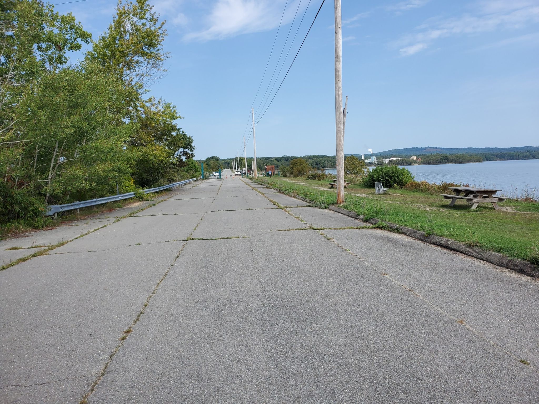 Paved road with power lines leading to a sunny lake with picnic tables. - Eastern Ledges Trail