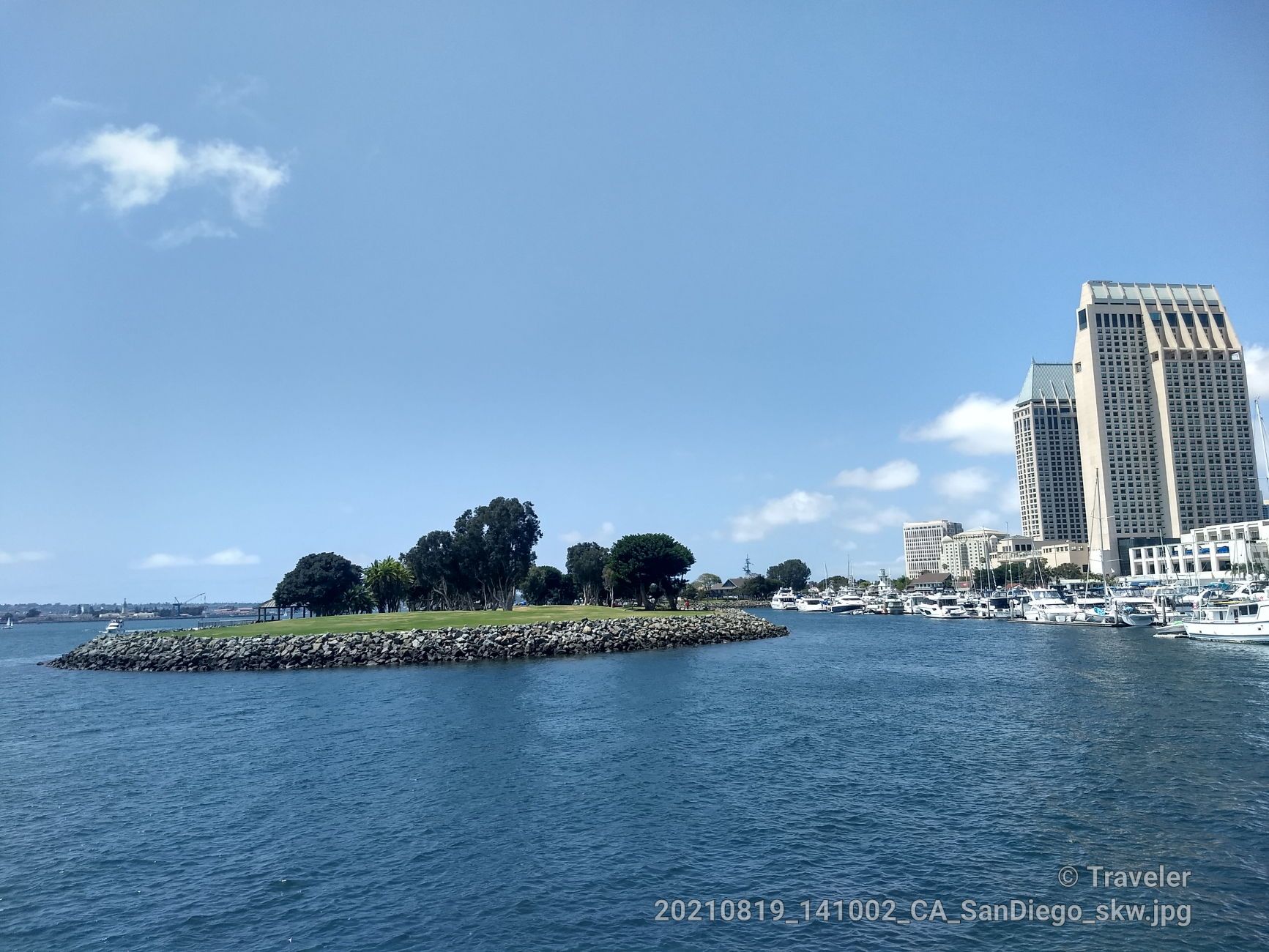 A small green island in a bay with city buildings and boats. - Embarcadero Marina Loop