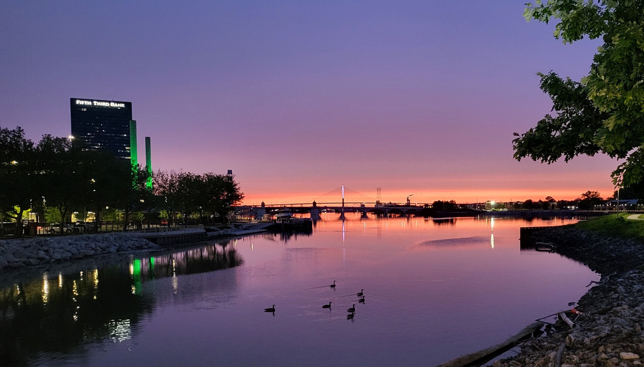 Vibrant purple and orange sunset over a river with city buildings and ducks. - Promenade Park – Middlegrounds Metropark loop from Toledo