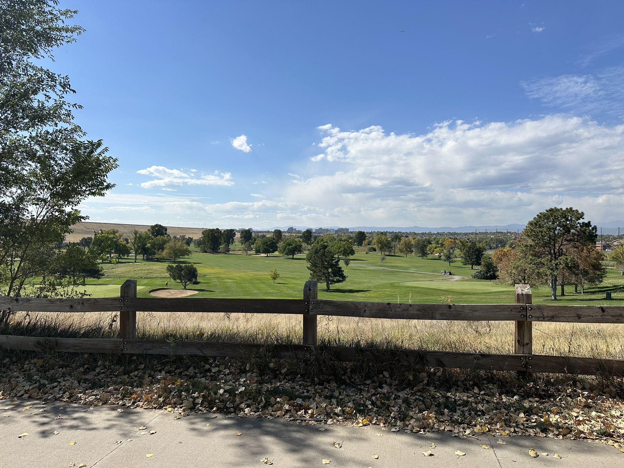 A green golf course with trees, viewed over a wooden fence. - Cherry Creek Reservoir – View of Cherry Creek Reservoir loop from Central Park