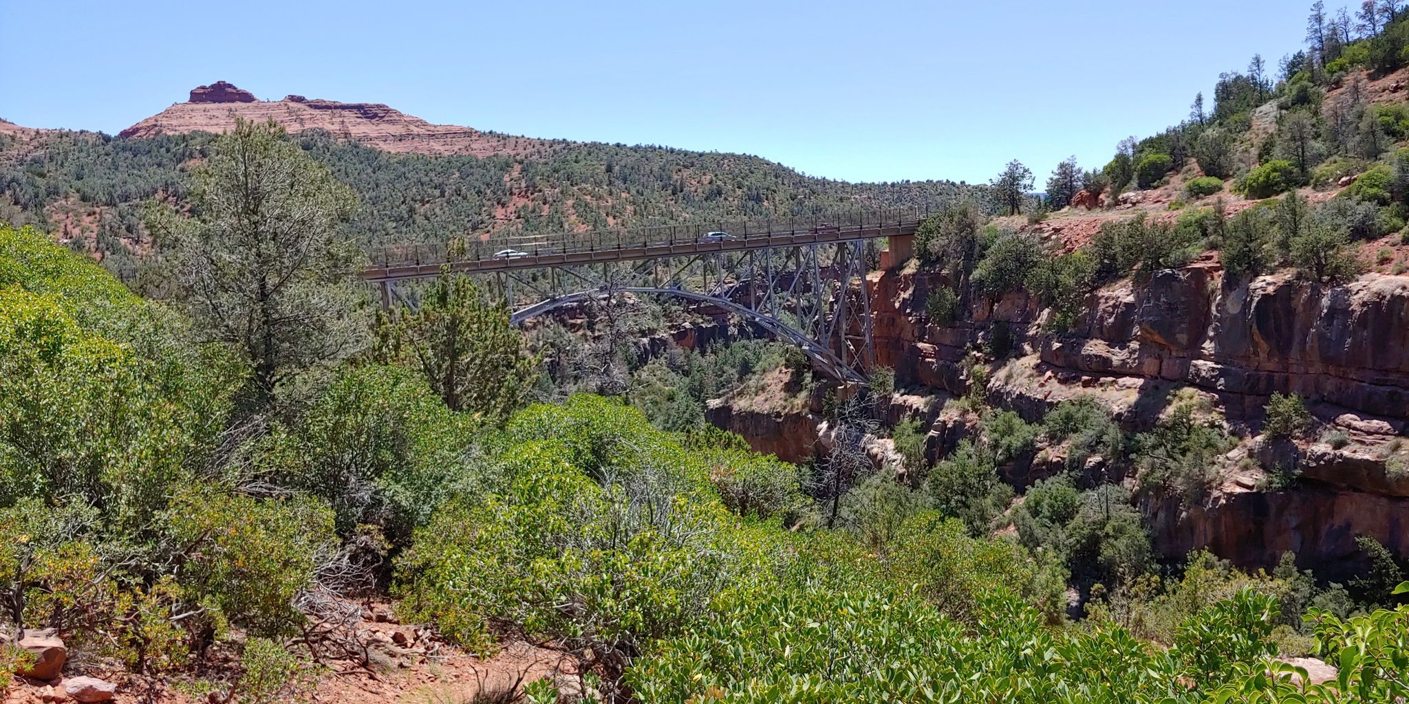 A large metal bridge spanning a deep canyon with green trees under a clear sky. - View of The Fin loop from Sedona