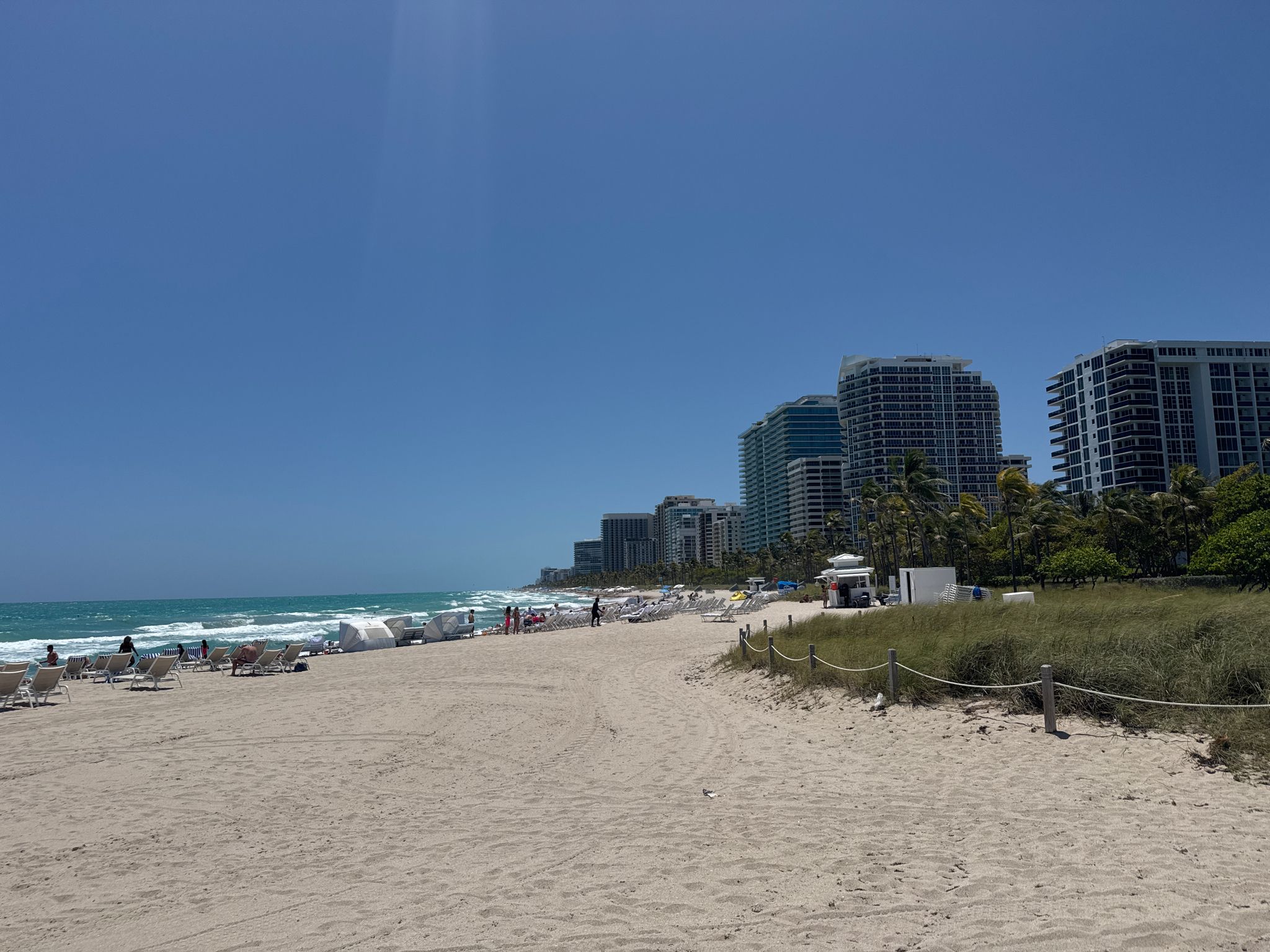Sunny beach with ocean, distant city buildings, and scattered people. - Bal Harbour Pier – Baker's Haulover Inlet loop from Surfside