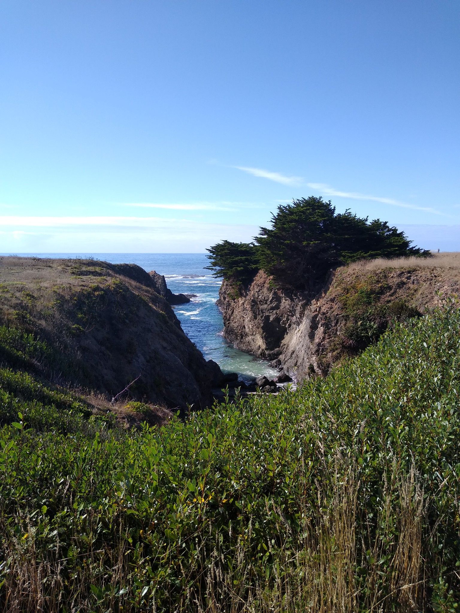 Coastal cliffs with a narrow inlet of blue ocean water under a clear sky. - Agate Beach Cove – Point Cabrillo Light Station loop from Mendocino