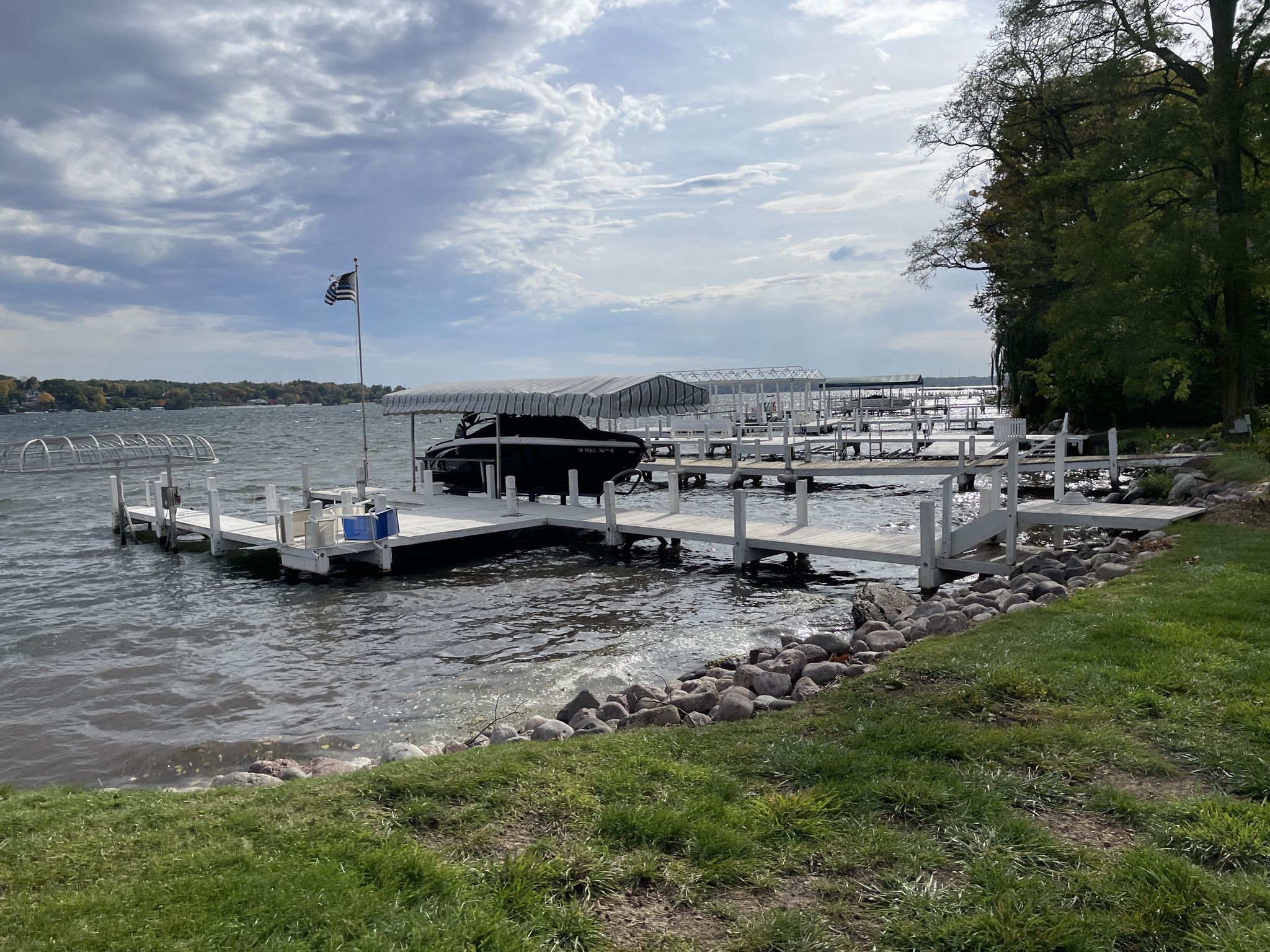 White wooden docks with a covered boat and flag on a rocky, grassy shore. - Big Foot Beach State Park – Riviera Beach loop from Lake Geneva