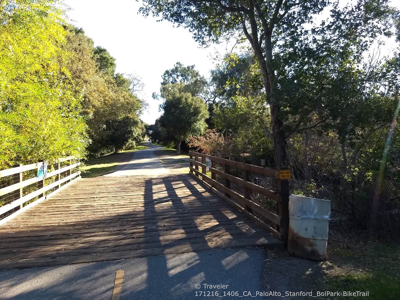 A wooden bridge crosses a paved path, casting shadows in bright sunlight. - Bol Park Loop