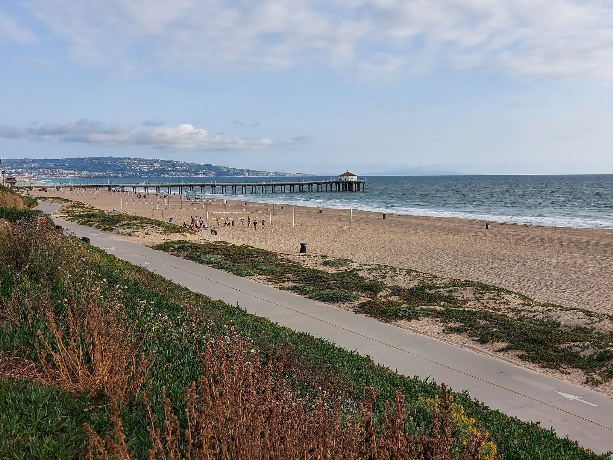 Beach with a long pier, ocean, paved path, and distant people. - El Segundo Beach – El Segundo Beach loop from El Segundo