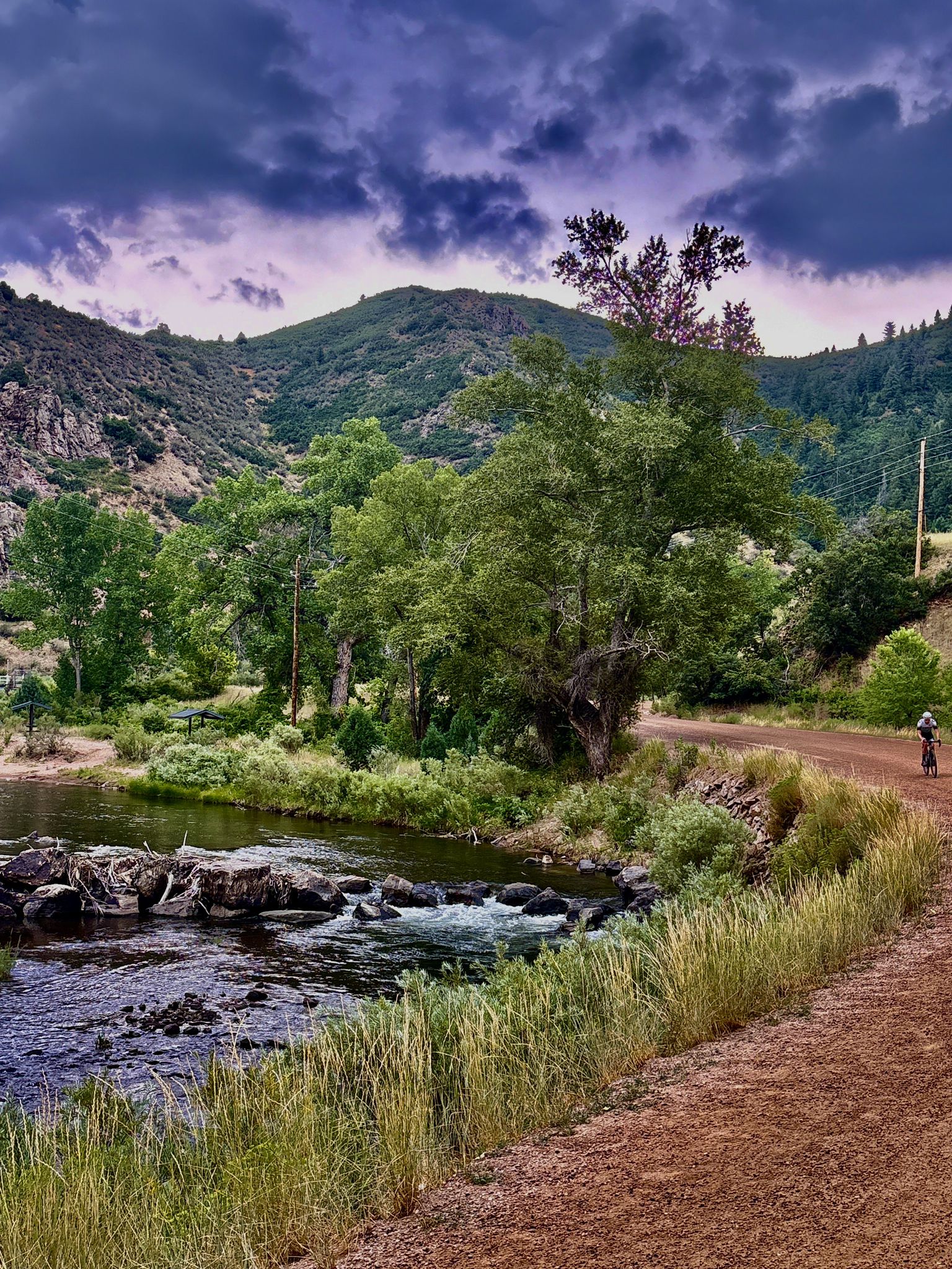 River and dirt road in a valley with a distant cyclist under dramatic clouds. - Waterton Canyon Trail via Colorado Trail