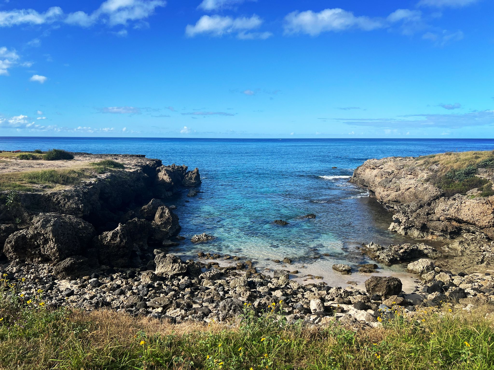 Clear blue ocean inlet surrounded by rocky cliffs and green vegetation. - Farrington Highway to Kaʻena Point State Park