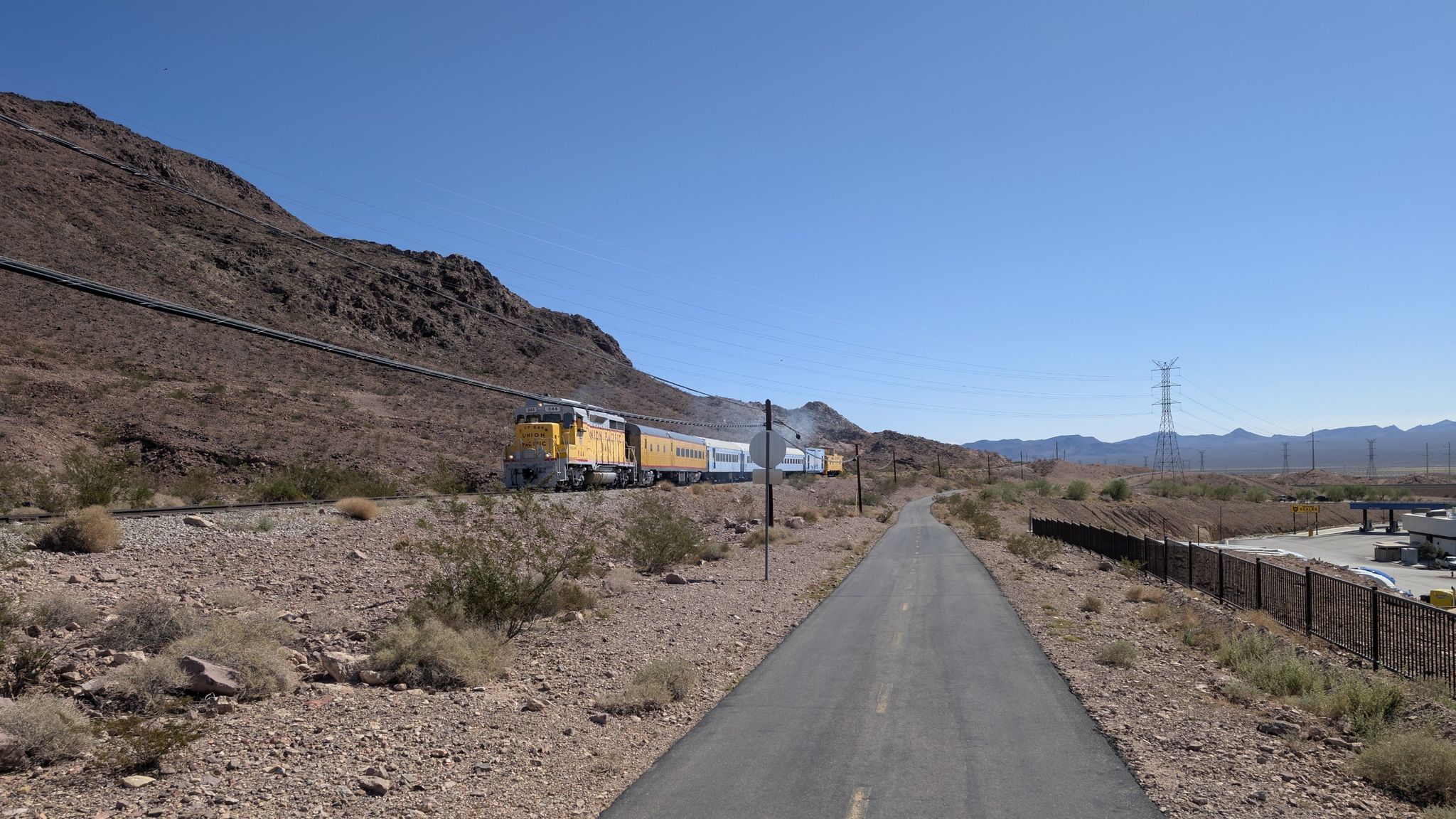 Long train on tracks beside a paved path in a dry, mountainous landscape. - Boulder Theatre – Boulder Dam Hotel loop from Clark County Museum
