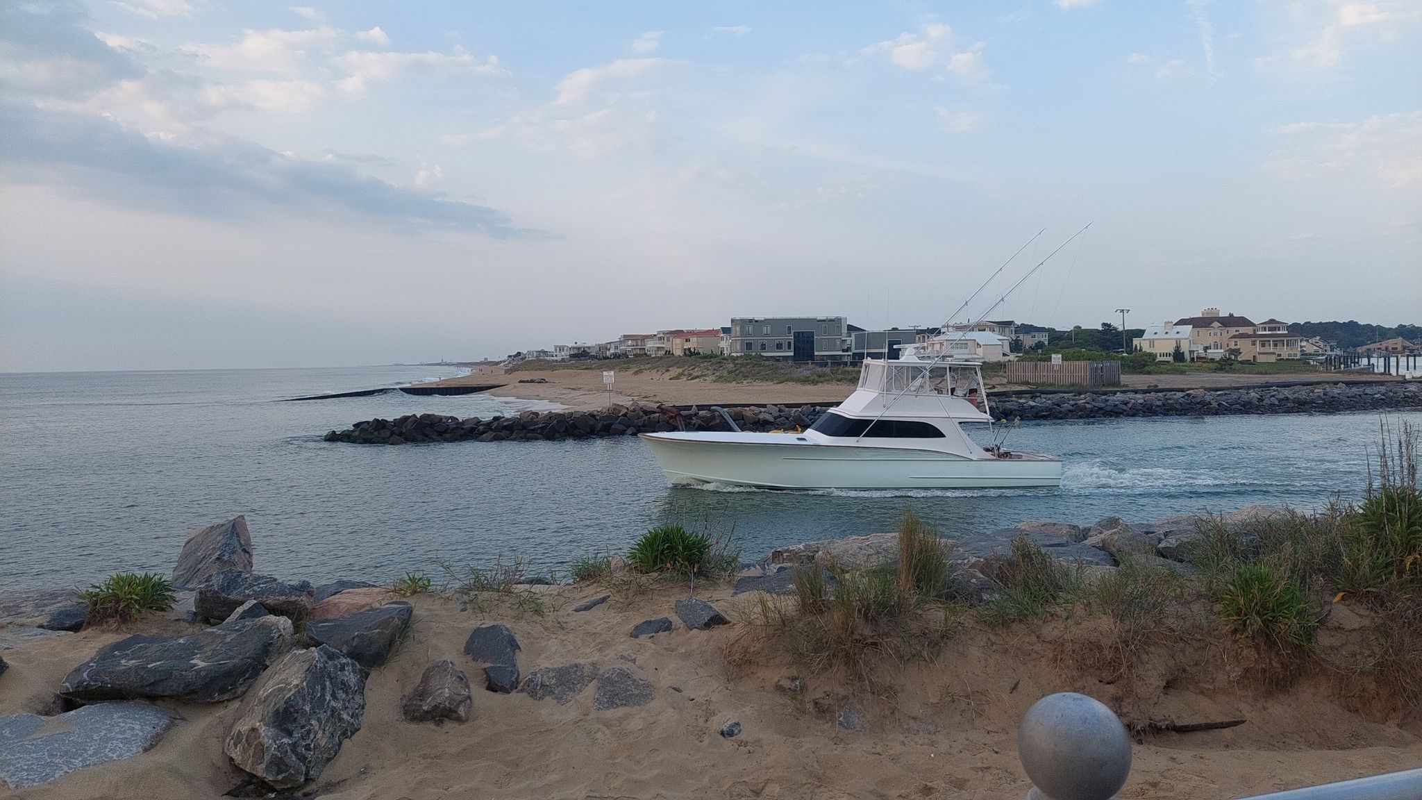 White boat moving through a channel between rocky shores under a cloudy sky. - Rudee Inlet loop from Virginia Beach