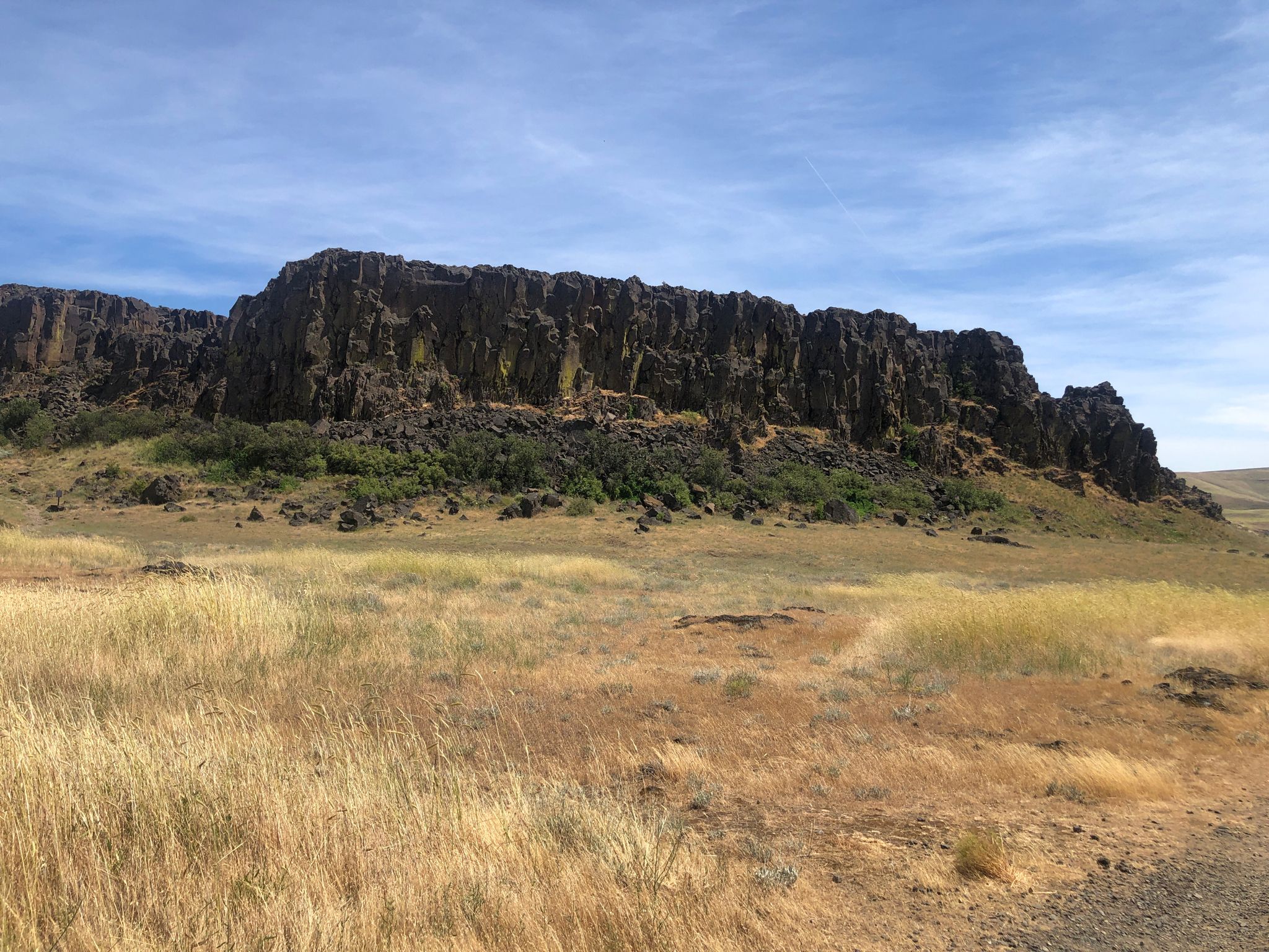 Expansive dry field before a long, dark rock cliff under blue sky. - Horsethief Butte Trail